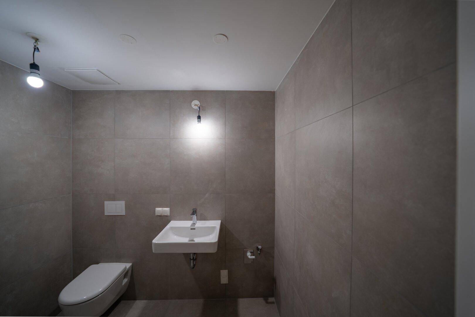 Modernes Gäste-WC mit Wand-WC und Waschbecken, komplett gefliest.