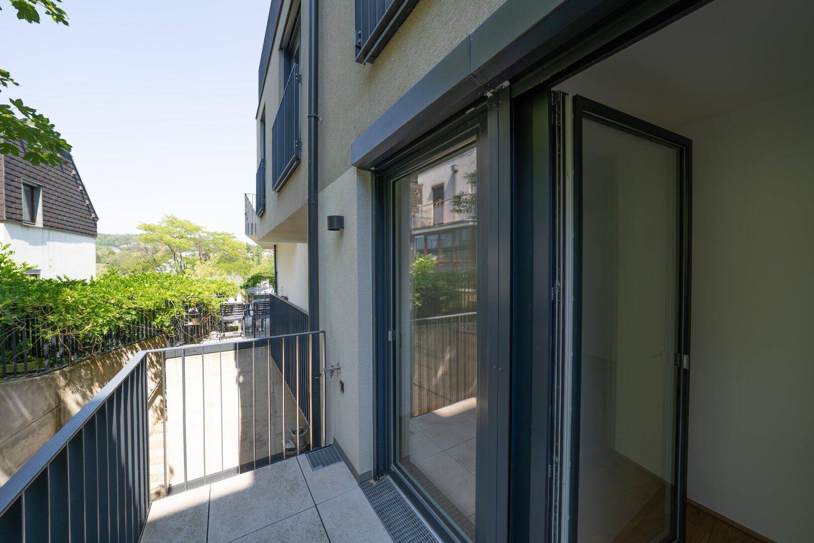 Moderner Balkon mit Fliesenboden und Metallgeländer, bietet einen Blick ins Grüne.