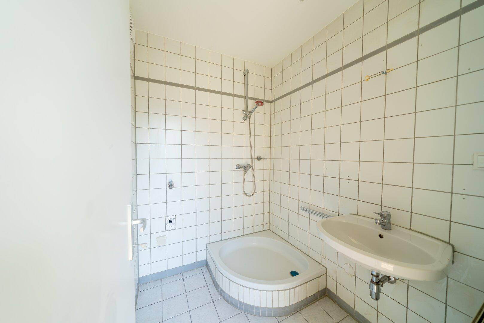 Gefliestes Badezimmer mit Eckdusche und Waschbecken in schlichtem Design.