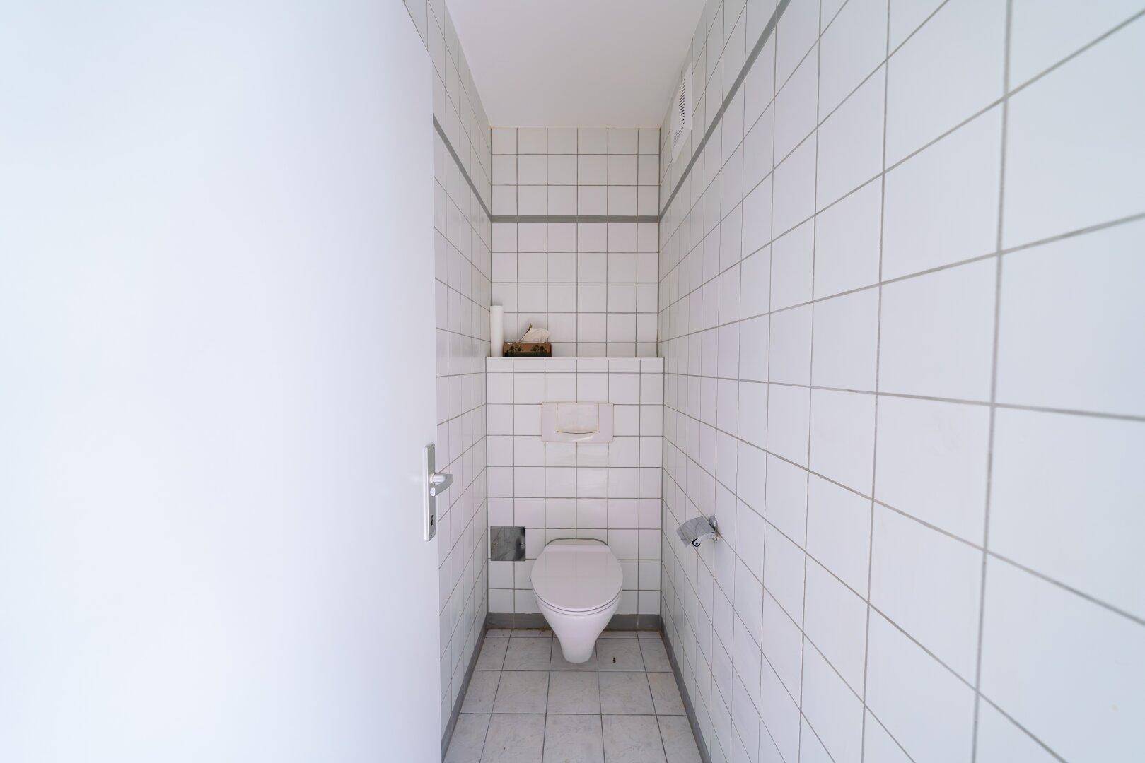 Kleines, hell gefliestes WC mit wandhängender Toilette.