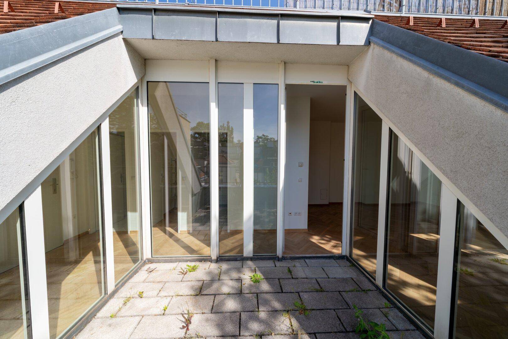 Kleine, sonnige Terrasse mit großen Glasfronten, die den Innenraum erhellen.