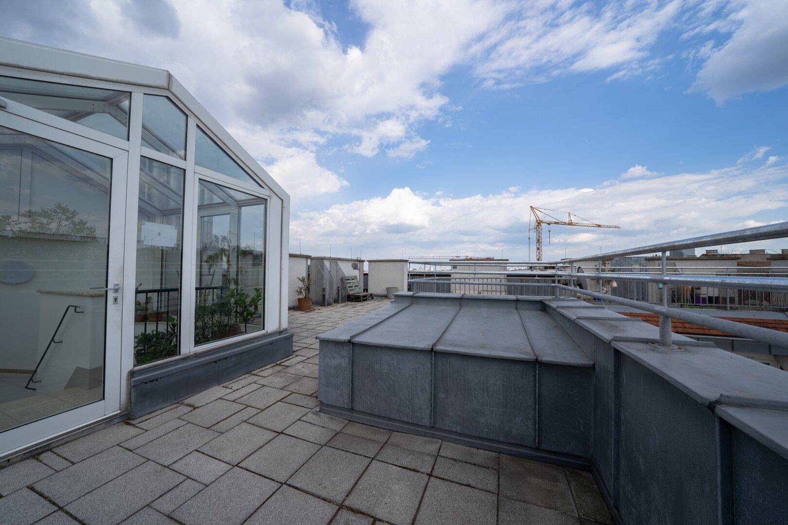 Weitläufige Dachterrasse mit Wintergarten und Blick auf den Himmel und die Umgebung.
