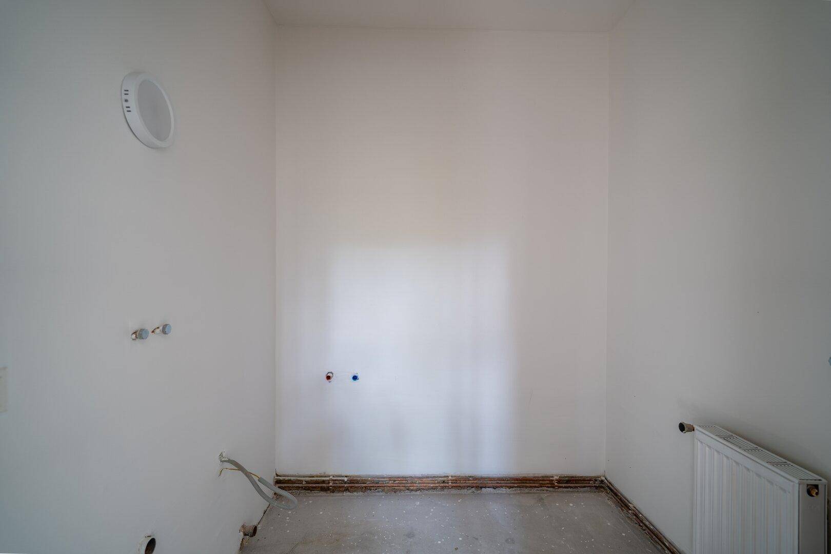 Leerer Badezimmerraum mit Anschlüssen für Sanitäranlagen und einem Lüftungssystem.