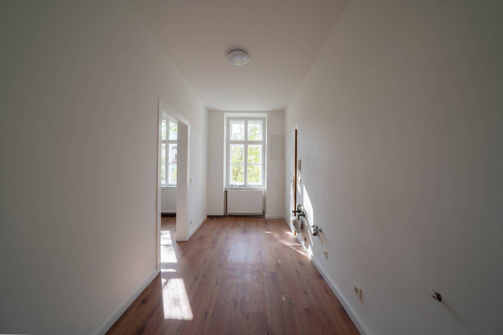 Langer, heller Flur mit Holzboden und natürlichem Lichteinfall durch ein Fenster am Ende.