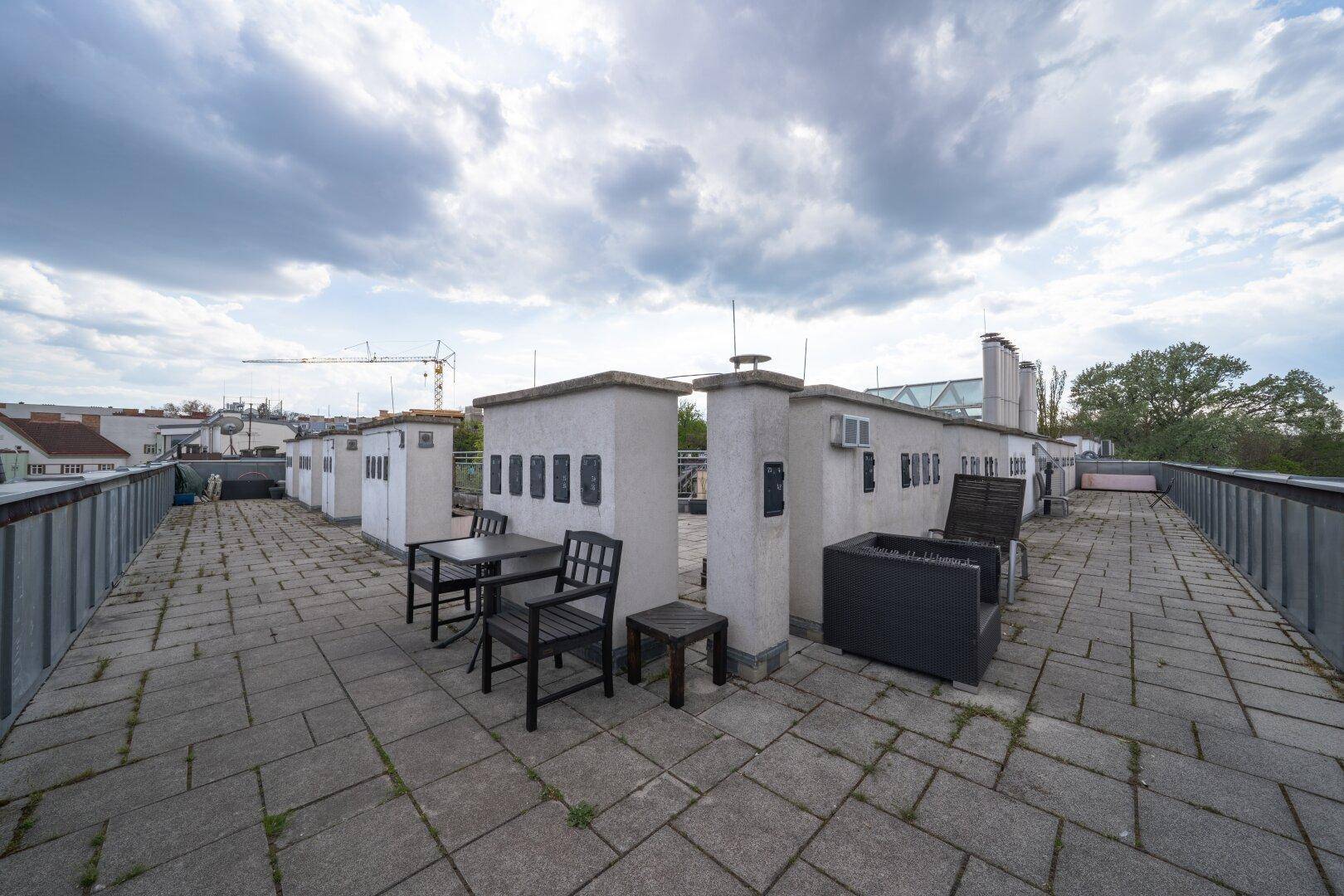 Große Dachterrasse mit Steinplatten, Sitzgelegenheiten und Blick auf die umliegende Stadt.