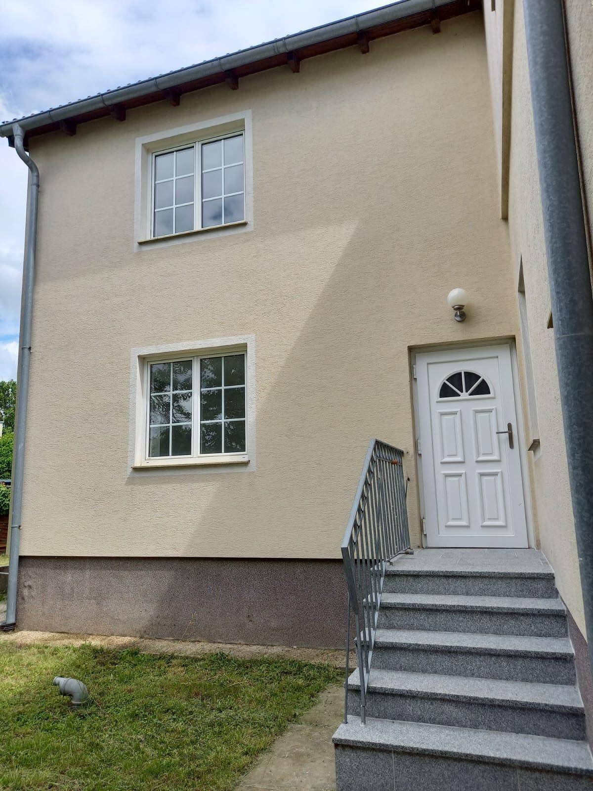 Seitenansicht des Hauses mit Eingangstür, Treppe und Fenstern im Obergeschoss.