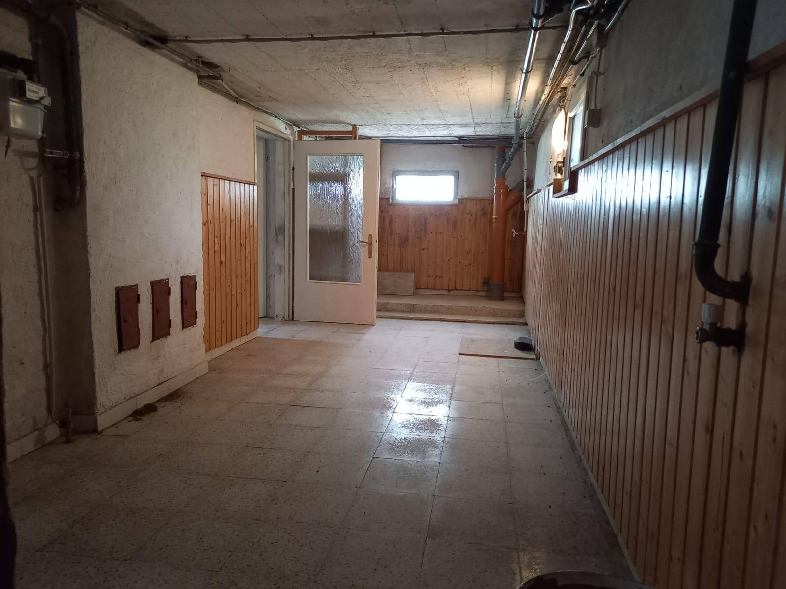 Kellerraum mit Fliesenboden, Holzverkleidung an den Wänden und einem kleinen Fenster.