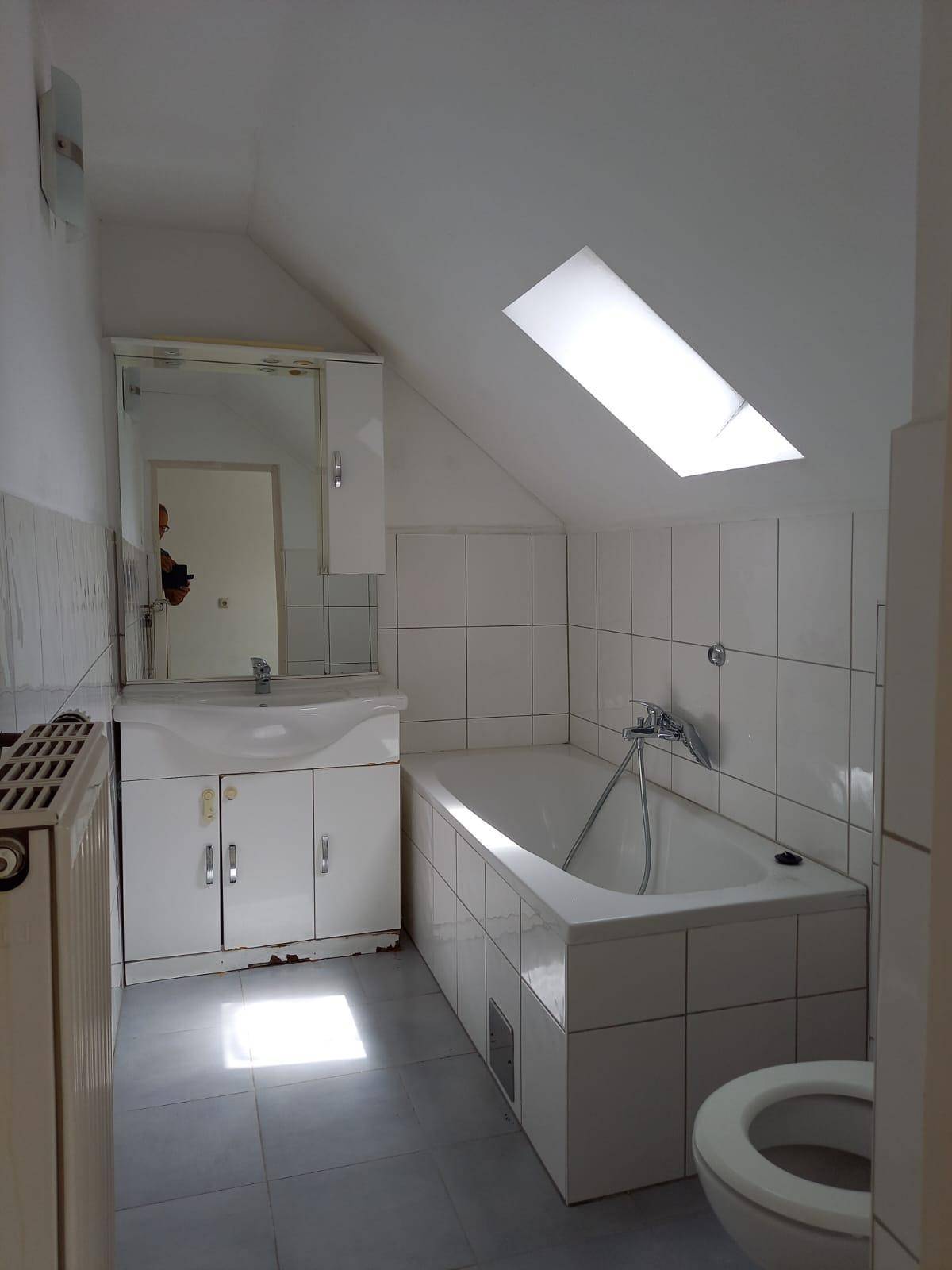 Badezimmer im Dachgeschoss mit Badewanne, Waschbecken und einem Dachfenster für Tageslicht.
