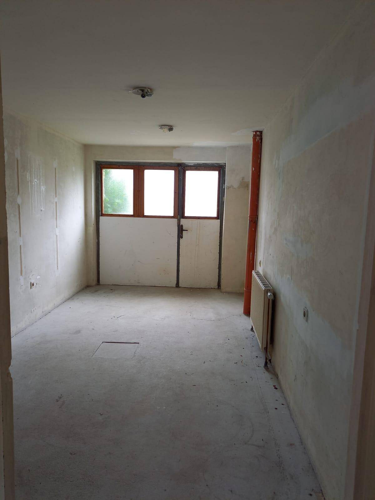 Unfertiger Raum mit Betonboden und großen Türen, bereit für den Ausbau.