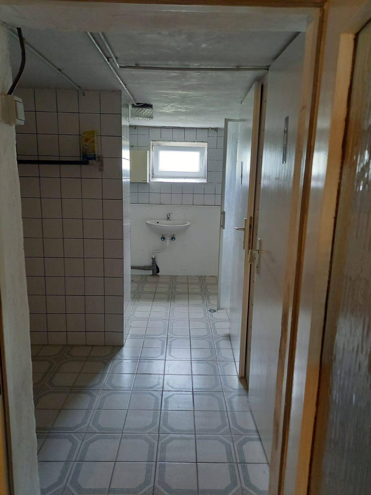 Einfaches Badezimmer im Keller mit Fliesen, Waschbecken und einem kleinen Fenster.