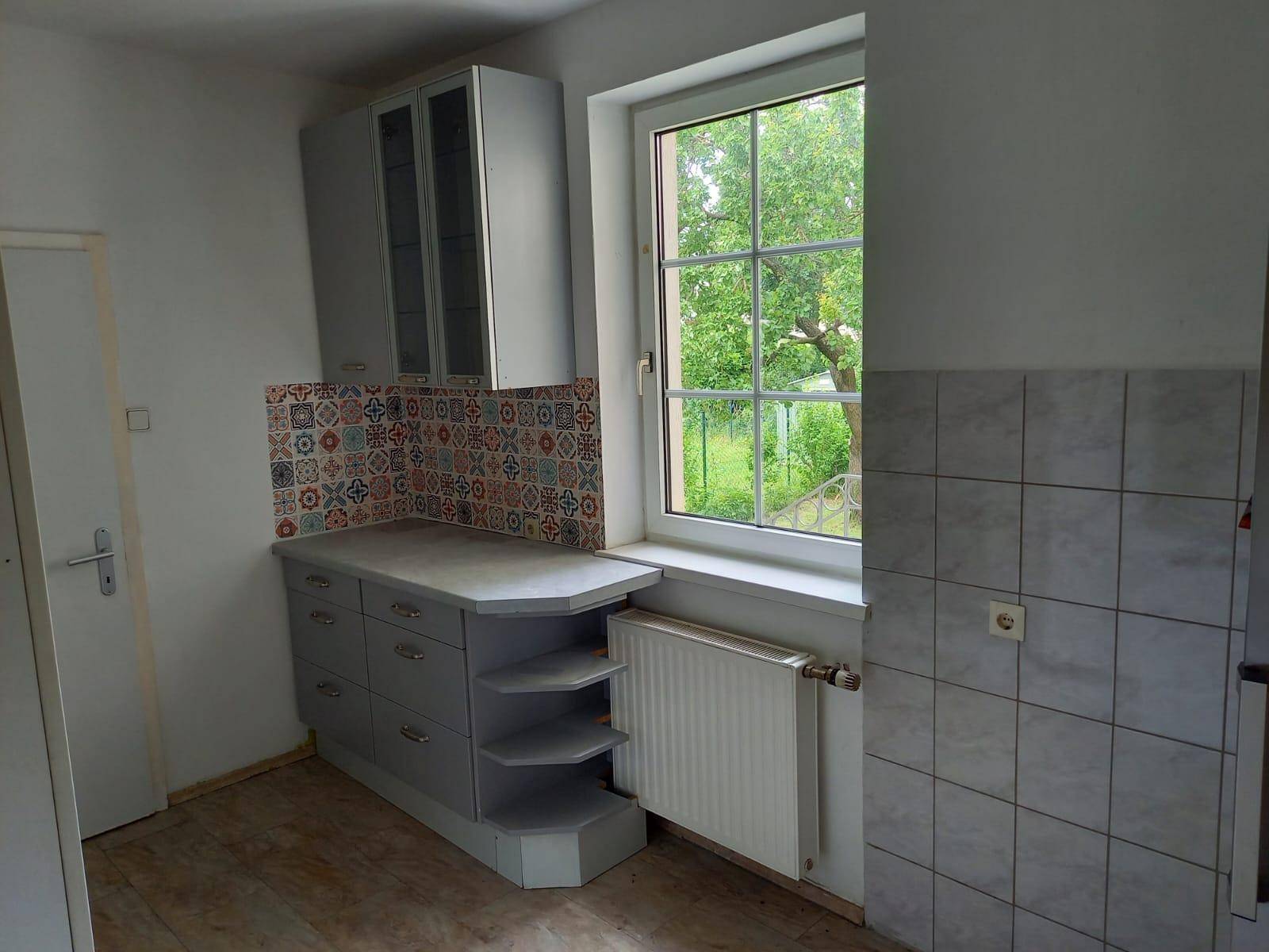 Küchenzeile mit Fenster, Heizkörper und farbenfrohen Fliesen, die den Raum beleben.