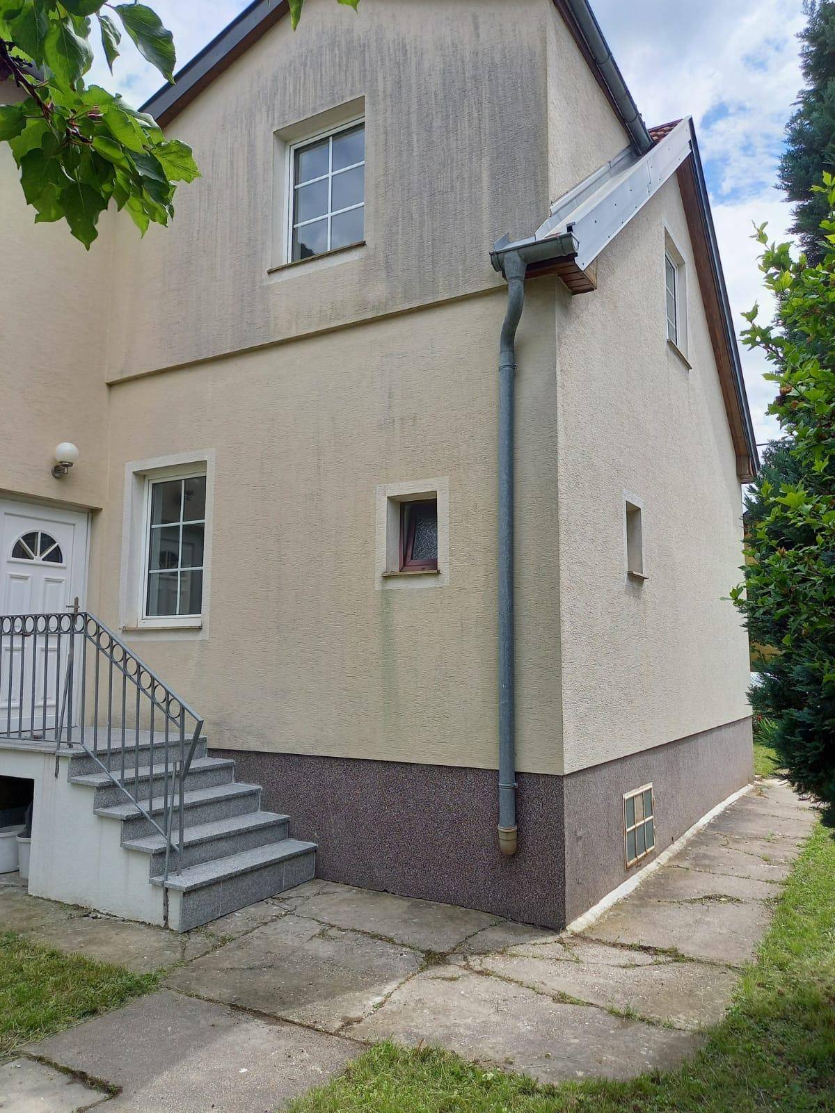 Seitenansicht des Hauses mit Eingangsbereich, Treppe und einem schmalen Weg entlang der Fassade.