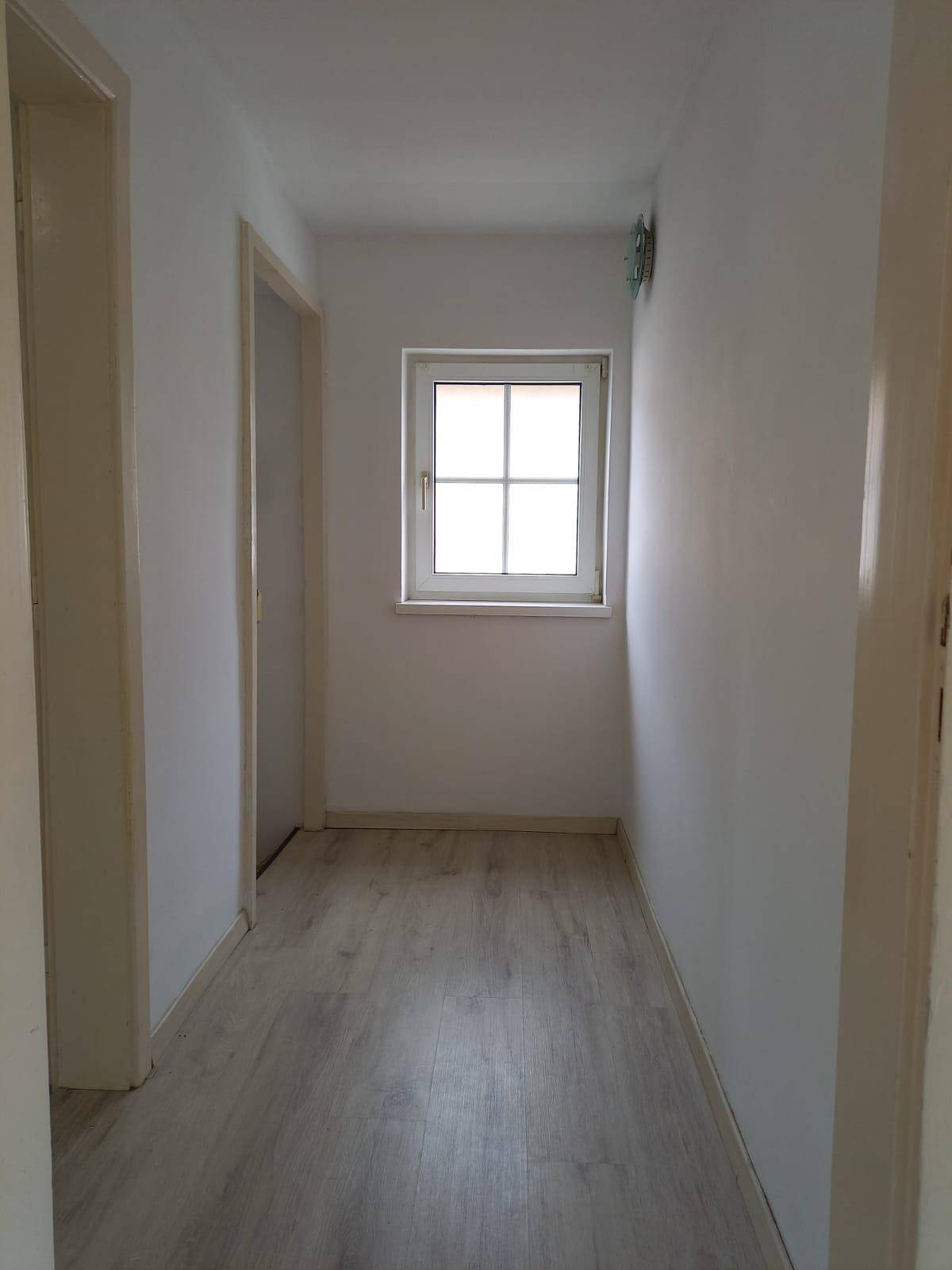 Heller Flur mit Laminatboden und einem Fenster, das Tageslicht hereinlässt.