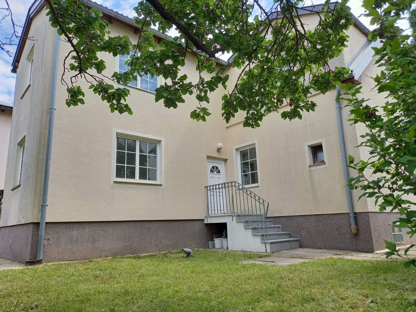 Rückansicht des Hauses mit Zugang zum Garten und altem Baumbestand im Hintergrund.