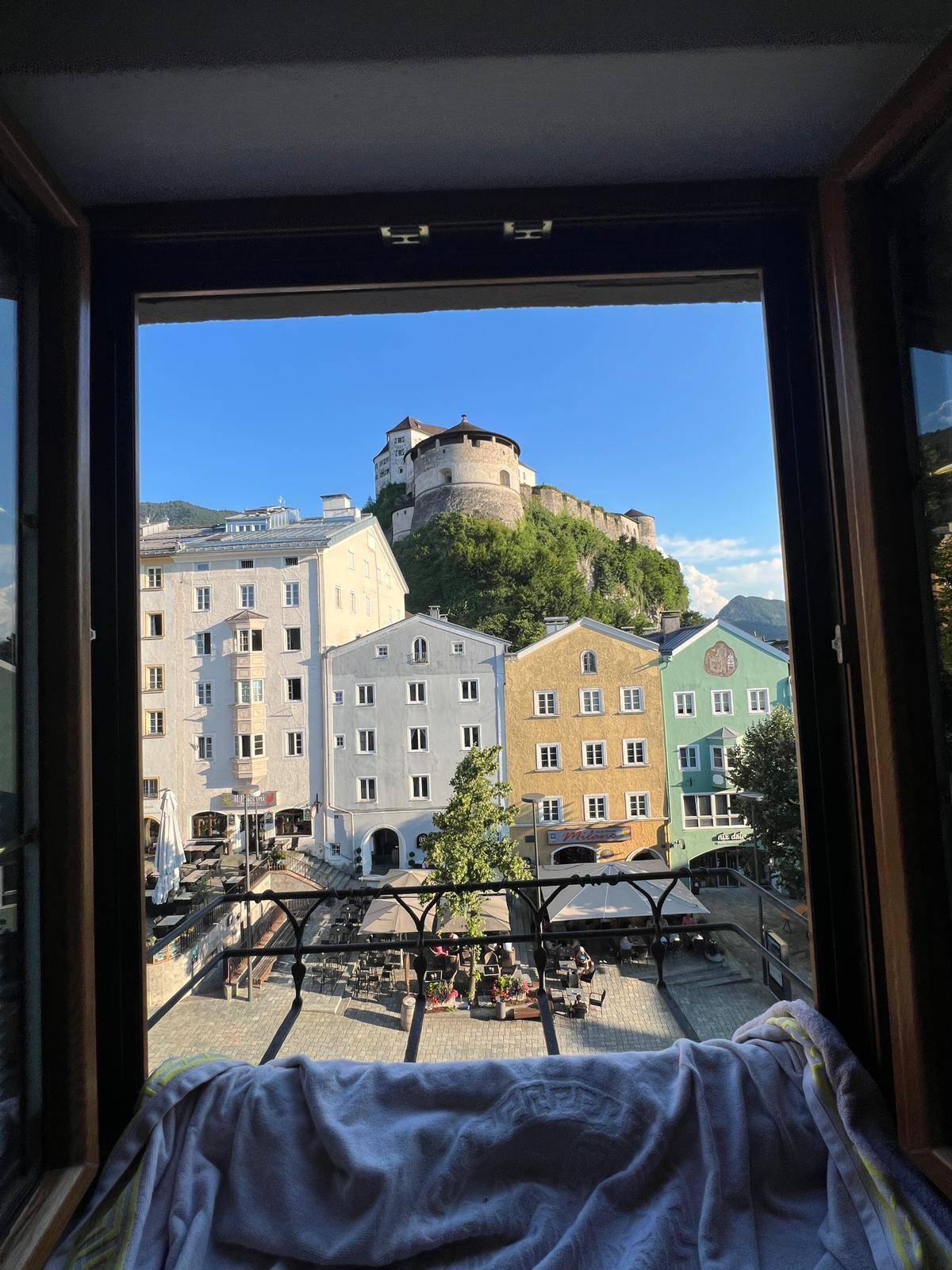 Malerischer Ausblick aus dem Fenster auf eine historische Stadt mit Burg auf dem Hügel.