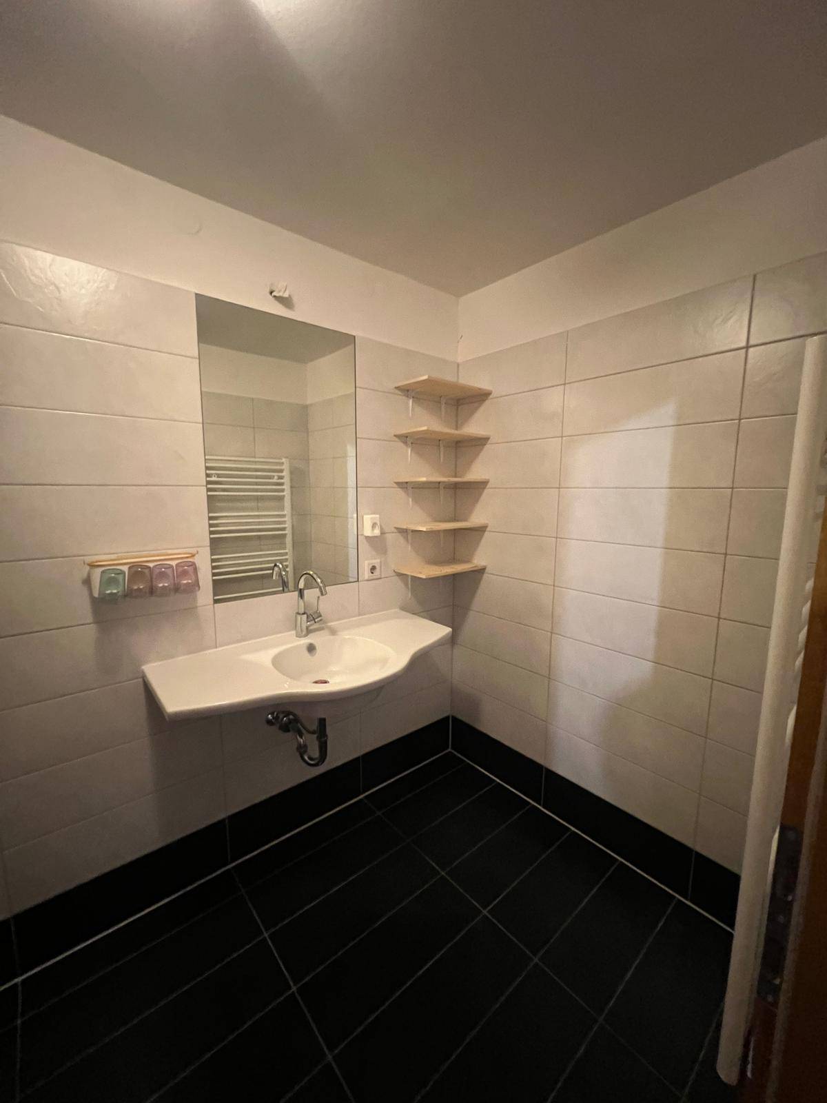 Modernes Badezimmer mit weiß gefliesten Wänden, schwarzem Boden und Einzelwaschbecken.