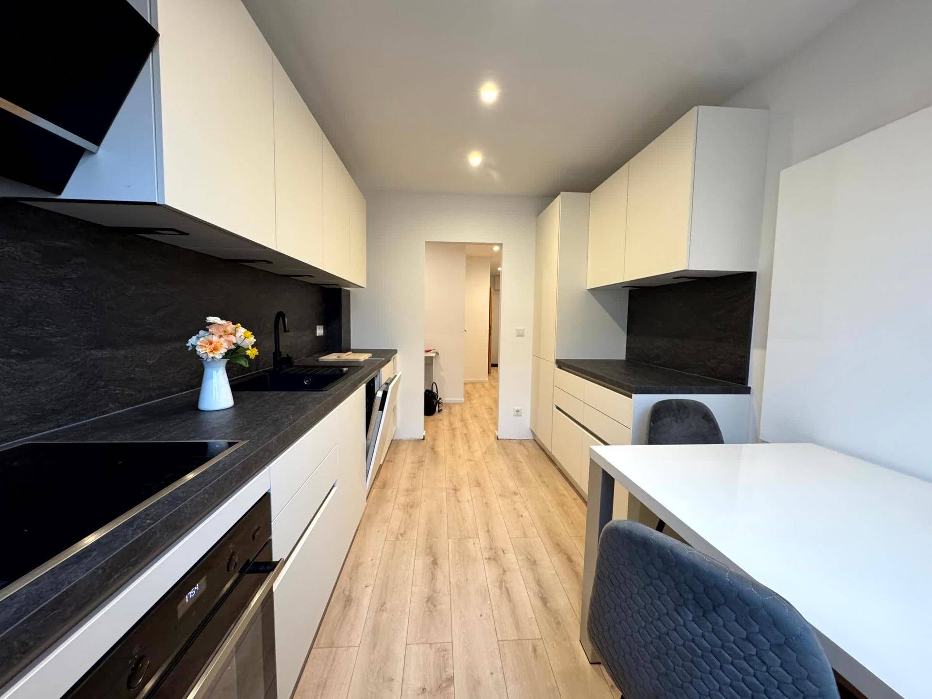 Moderne Einbauküche mit weißen Schränken, dunkler Arbeitsplatte und integriertem Essbereich.