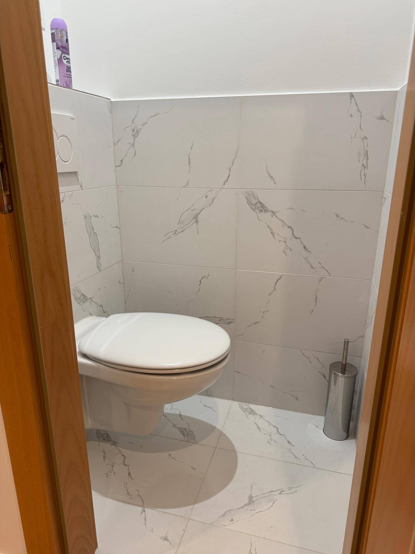 Separates WC mit wandhängender Toilette und modernen Fliesen in Marmoroptik.