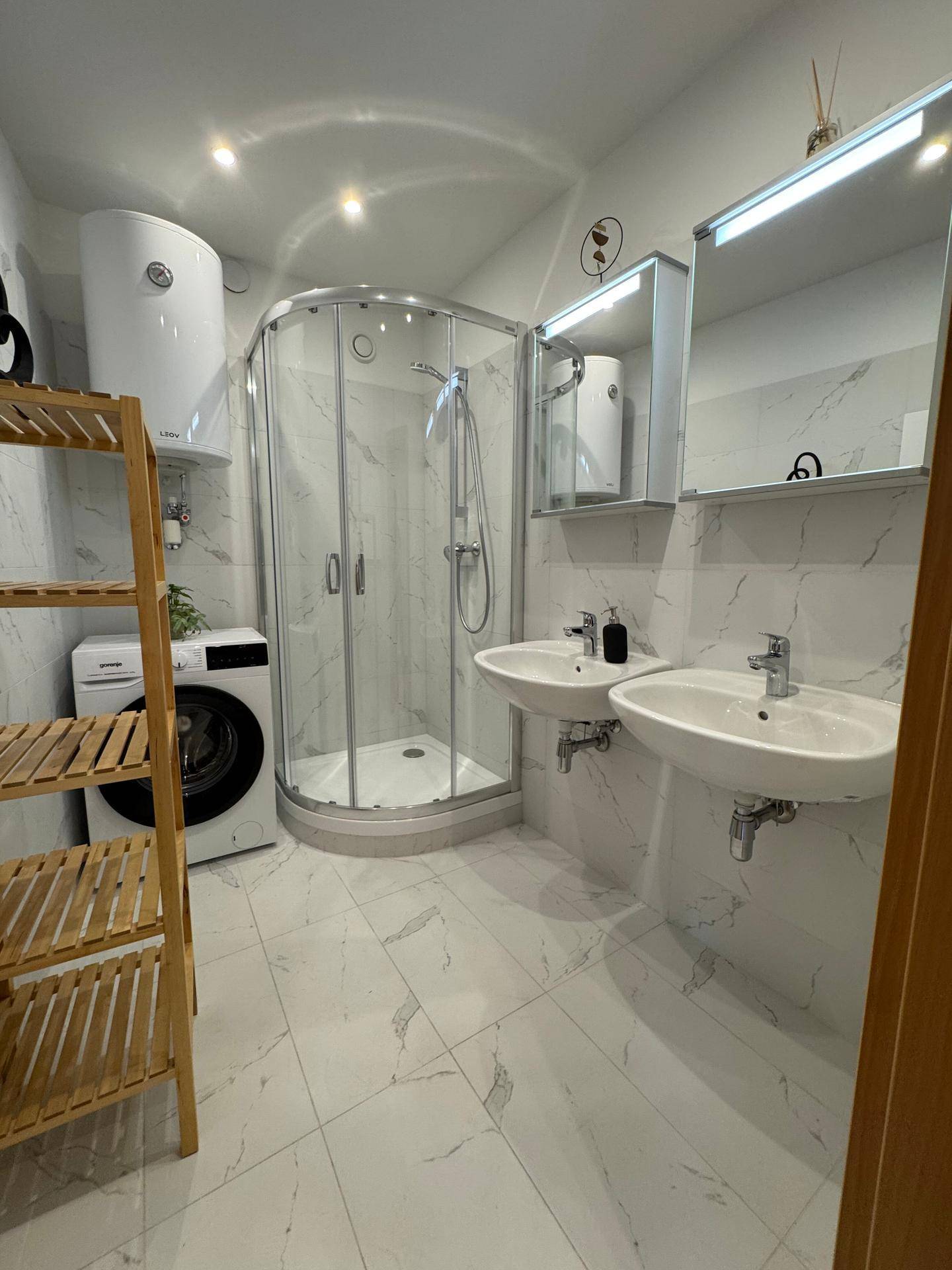 Modernes Badezimmer mit zwei Waschbecken, Duschkabine und integrierter Waschmaschine.