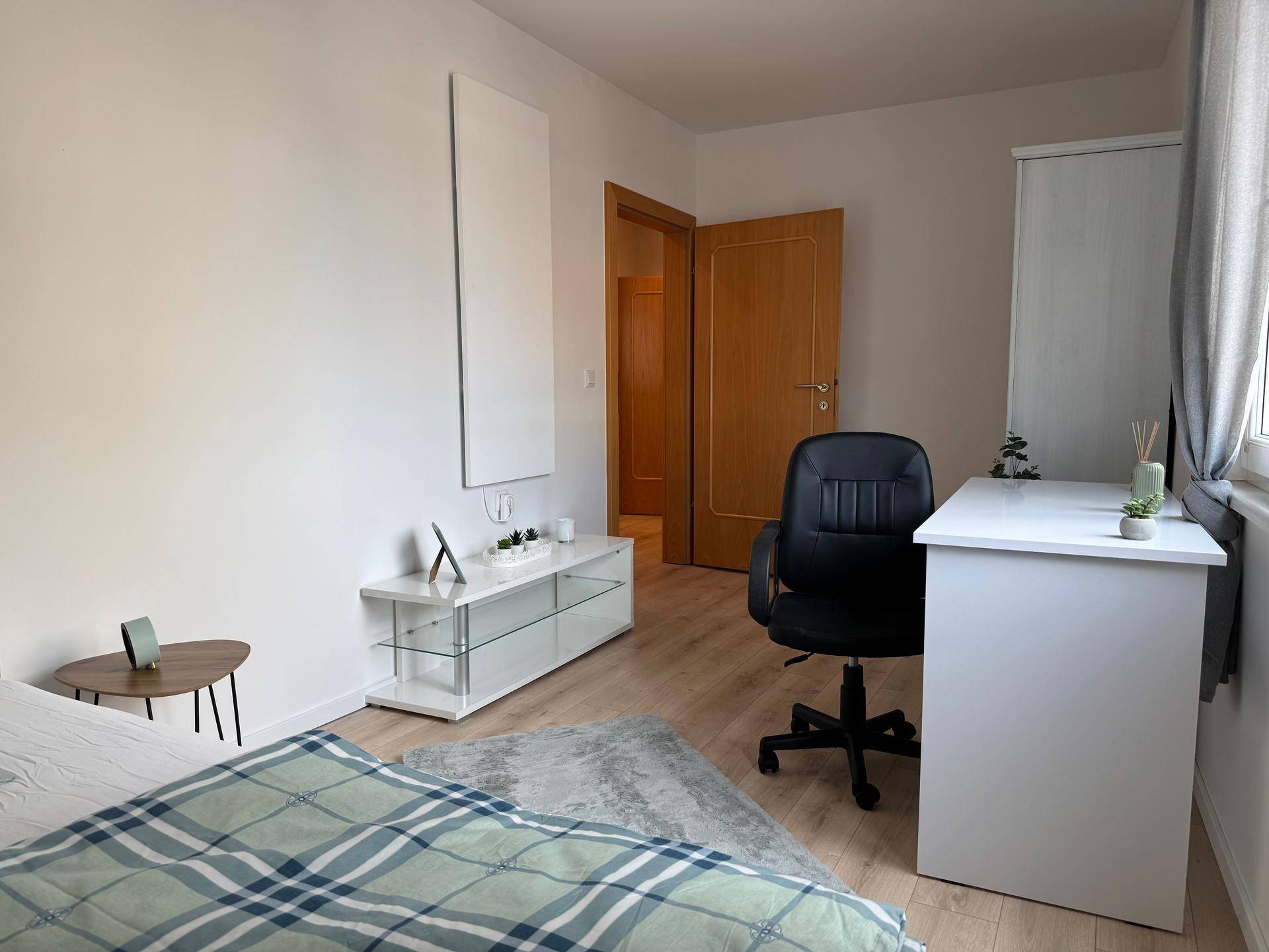 Modern eingerichtetes Schlafzimmer mit Schreibtisch, Bürostuhl und Zugang zum Flur.