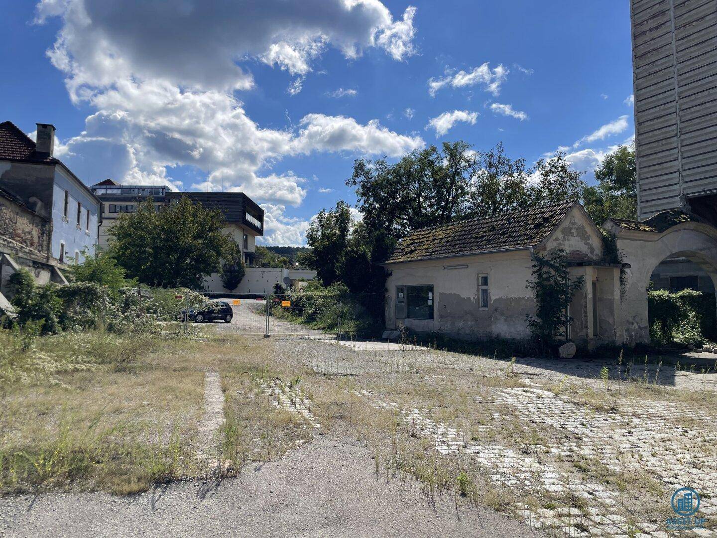Weitläufiges Gelände mit einem verfallenen Gebäude, Torbogen und einer großen, unbefestigten Fläche.