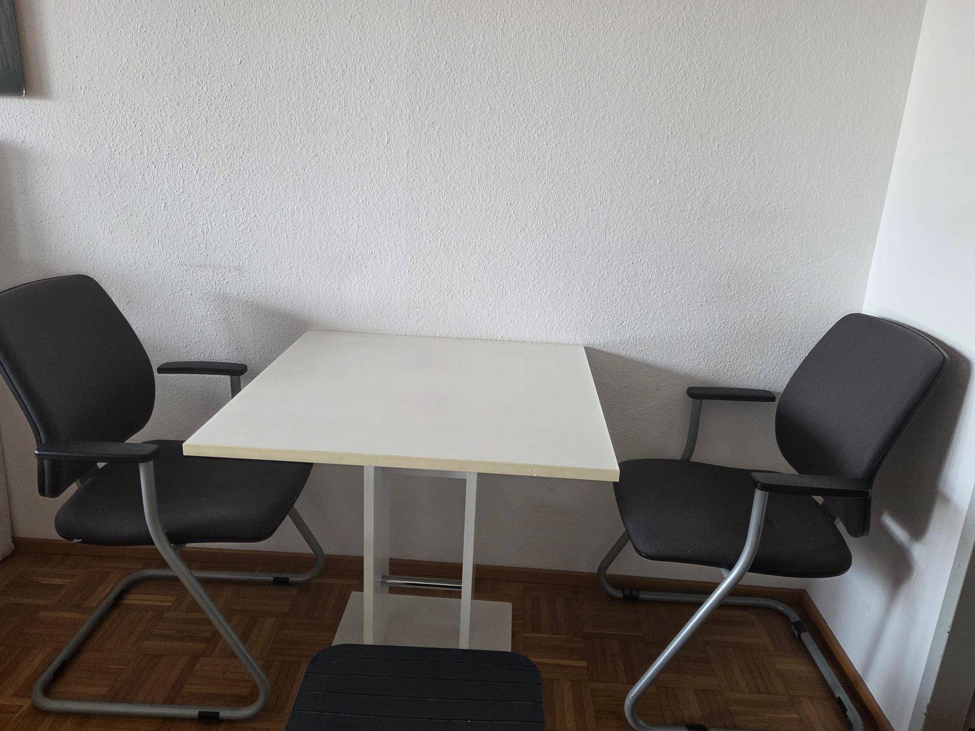 Kleiner Essbereich oder Arbeitsplatz mit zwei Stühlen und Parkettboden in einem hellen Raum.