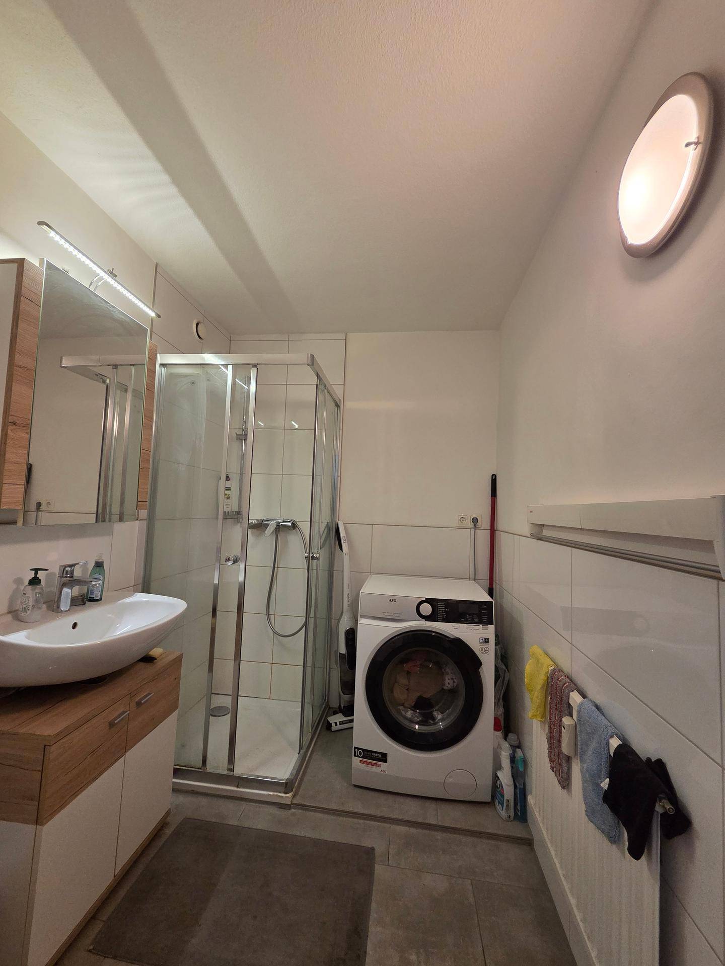 Modernes Badezimmer mit Duschkabine, Waschbecken und integrierter Waschmaschine.