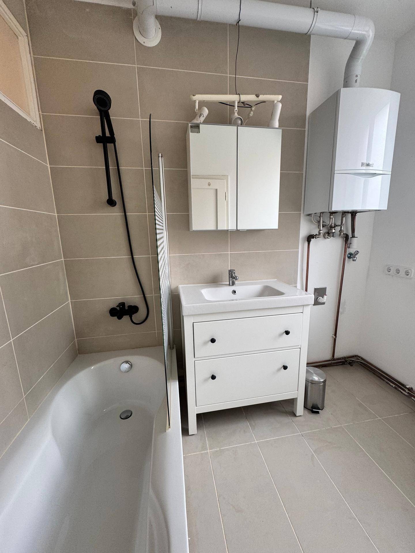 Modernes Badezimmer mit Badewanne, Einzelwaschbecken, Spiegelschrank und beigefarbenen Fliesen.