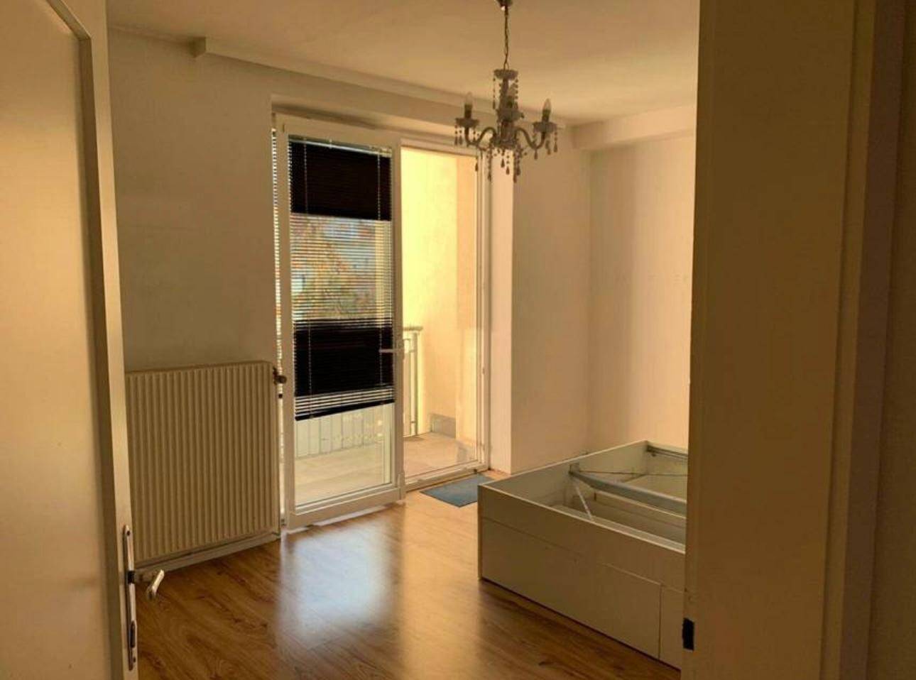 Schlafzimmer mit Laminatboden, einem Bettgestell und Zugang zu einem Balkon durch eine Glastür.