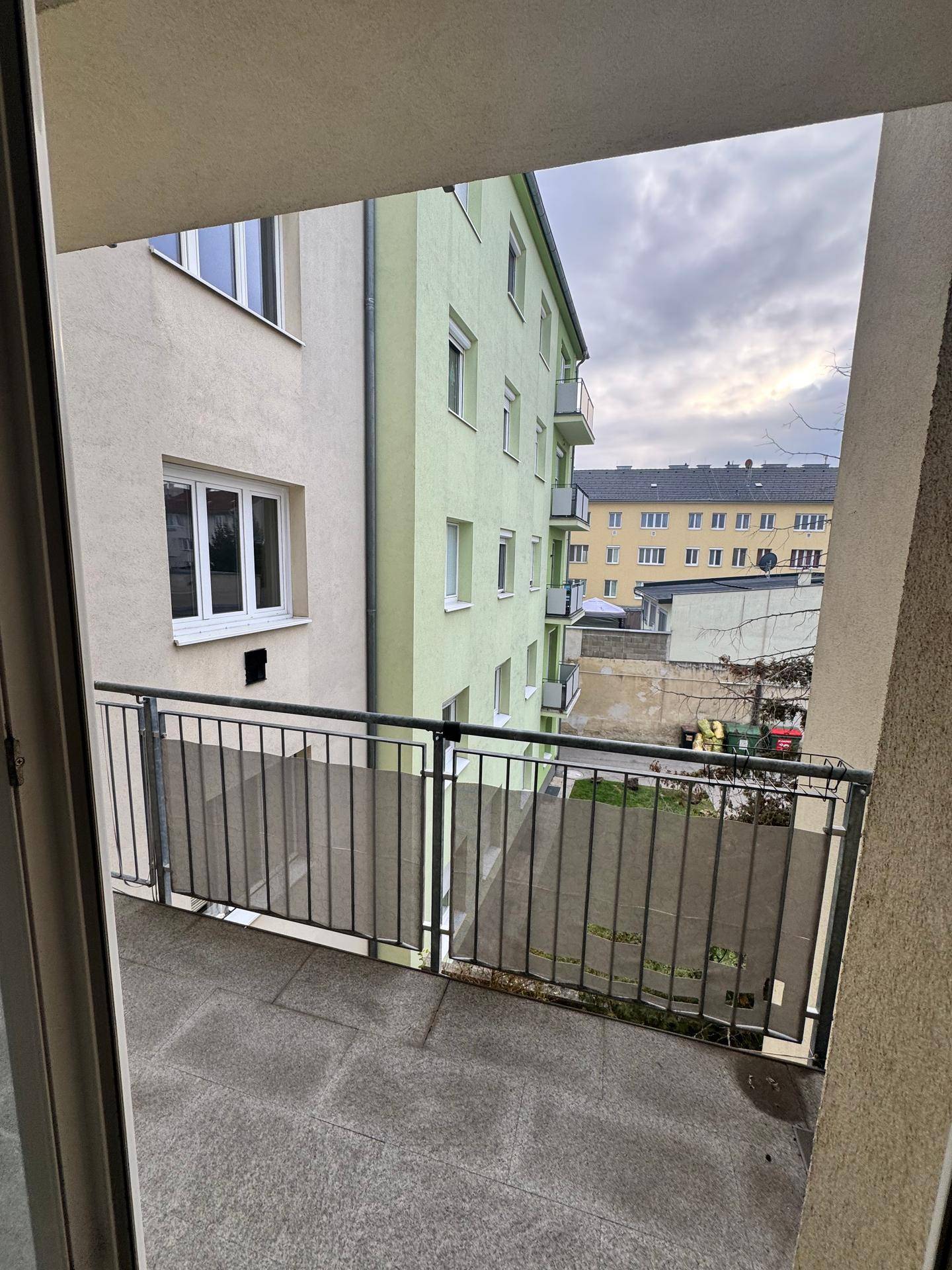 Blick von einem Balkon auf die umliegenden Gebäude und den Himmel, mit einer Metallbrüstung.