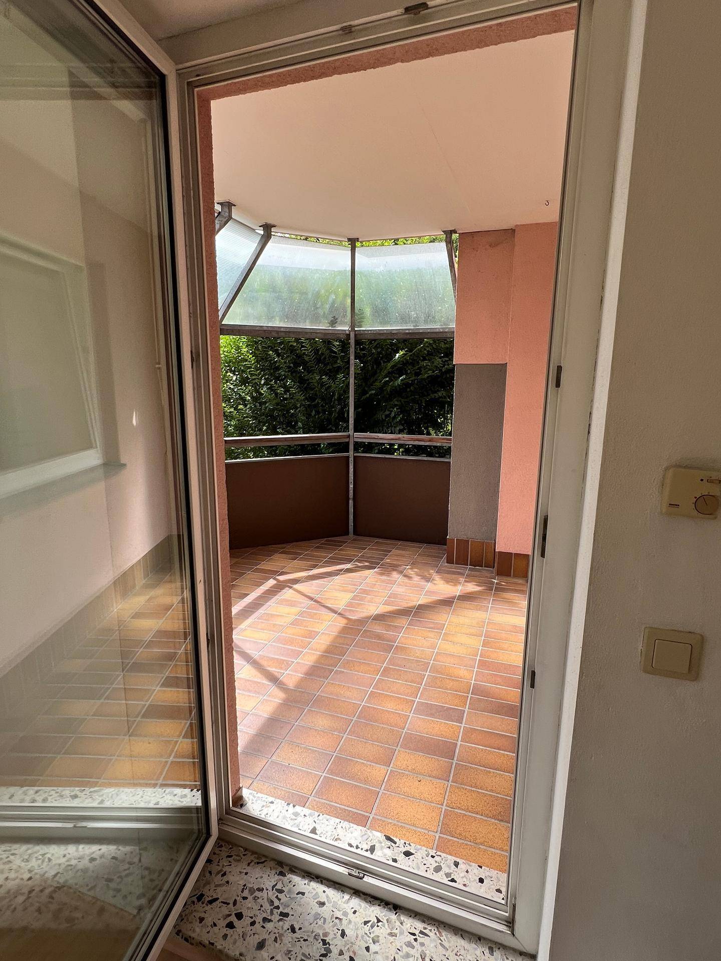 Verglaster Balkon mit Fliesenboden und Blick ins Grüne, ideal zum Entspannen.