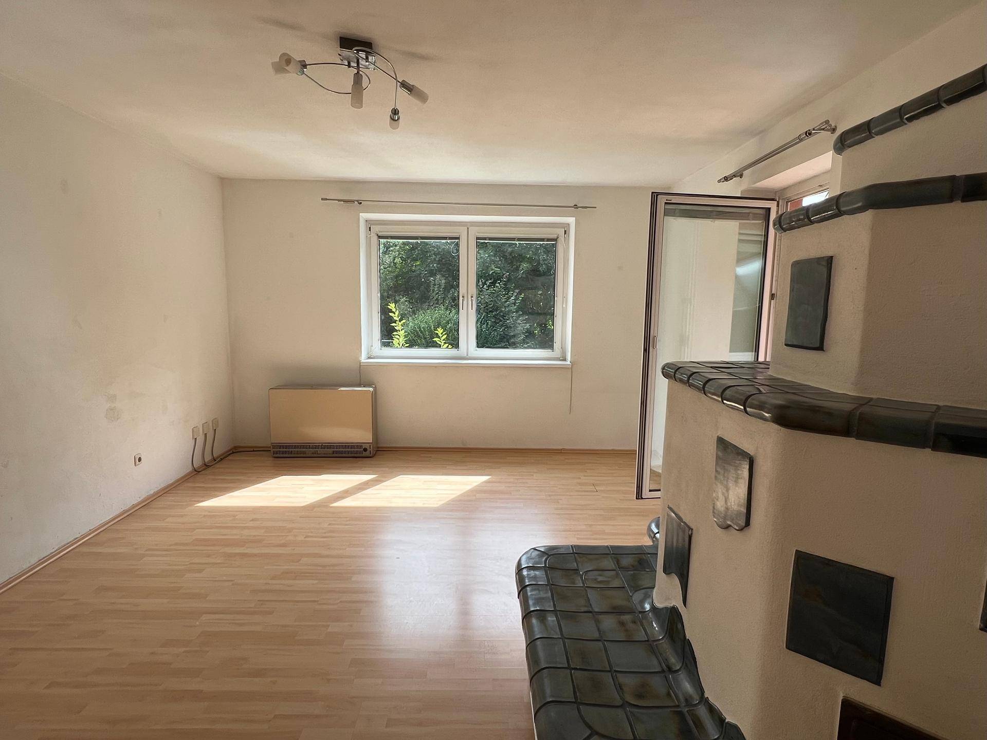 Helles Wohnzimmer mit Kachelofen, Laminatboden und Zugang zum Balkon.