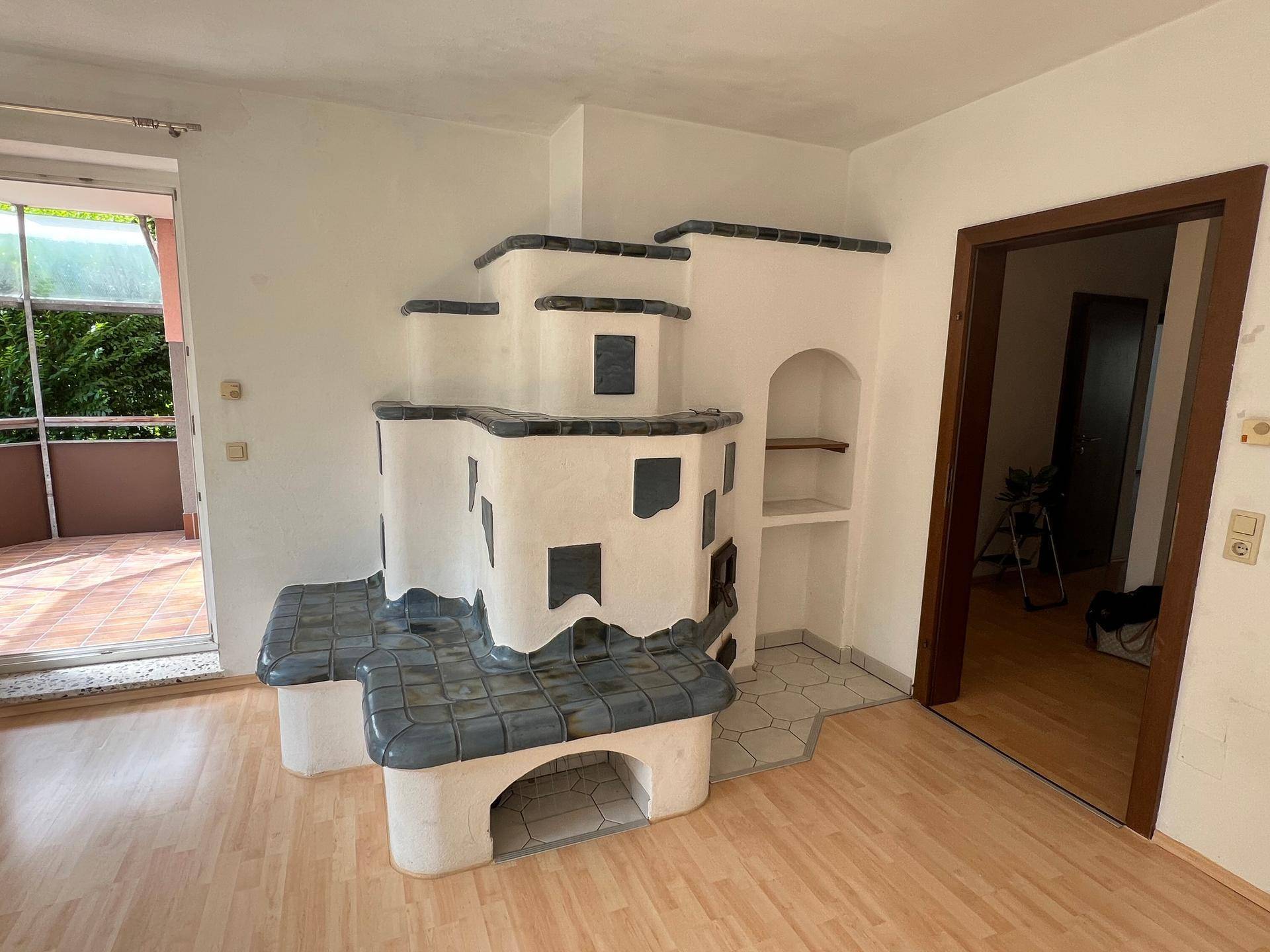 Gemütlicher Kachelofen im Wohnzimmer mit Sitzbank und Zugang zum verglasten Balkon.
