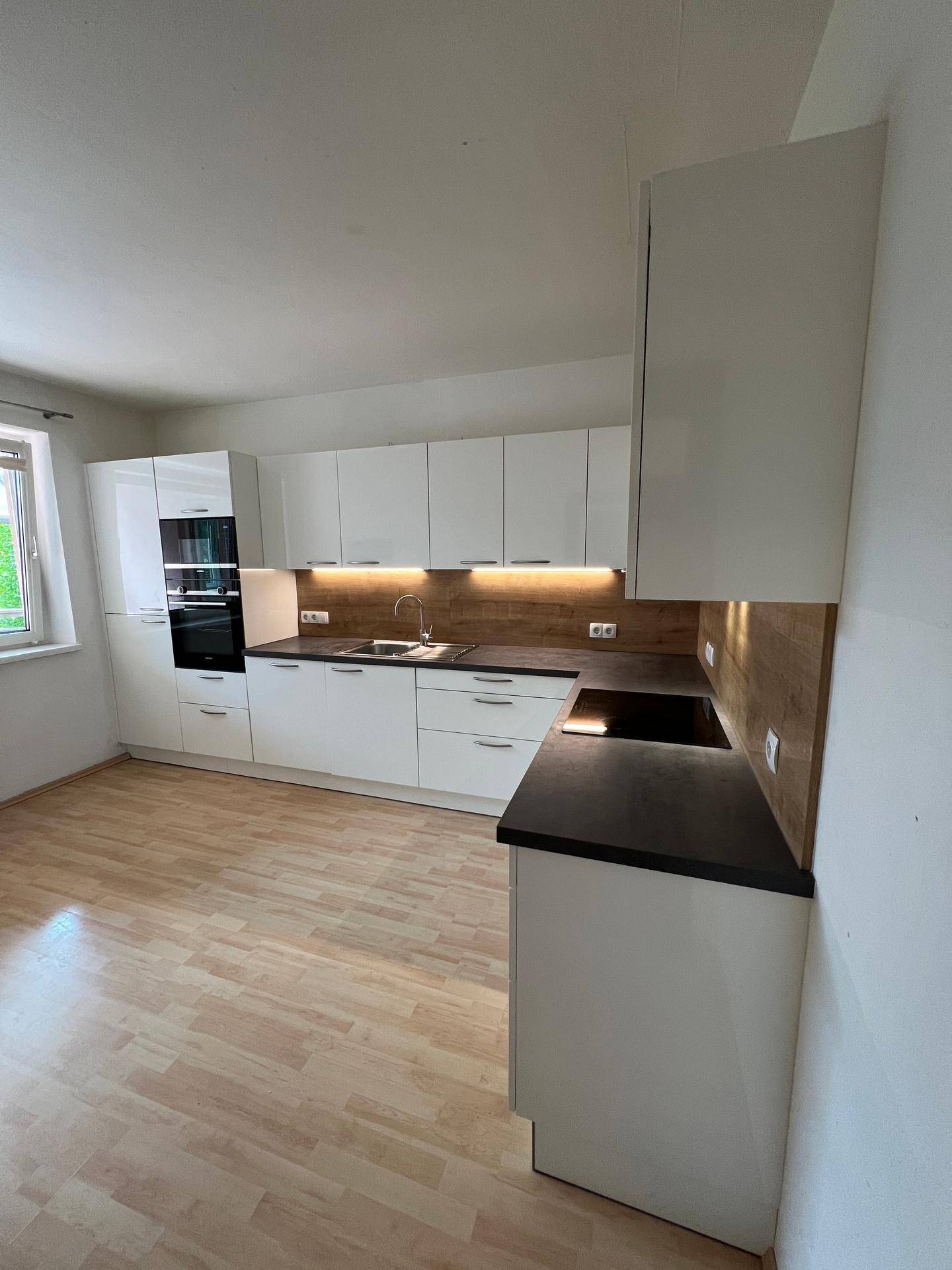 Helle, moderne Küche mit weißen Schränken, dunkler Arbeitsplatte und Laminatboden.