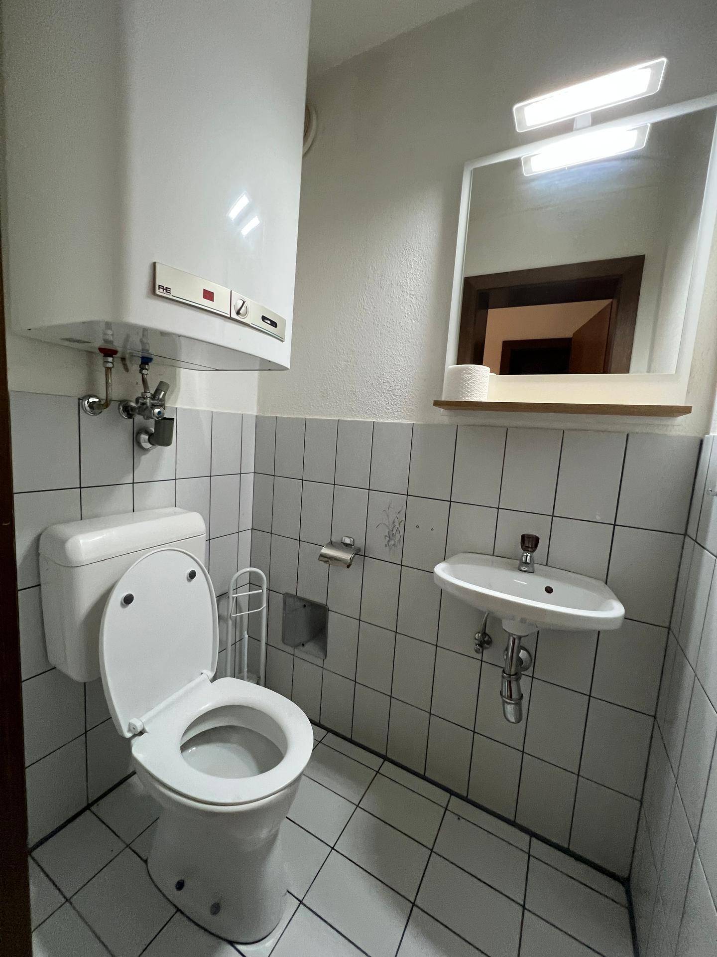 Kleines Gäste-WC mit Toilette, Waschbecken und Boiler, gefliest in Weiß.