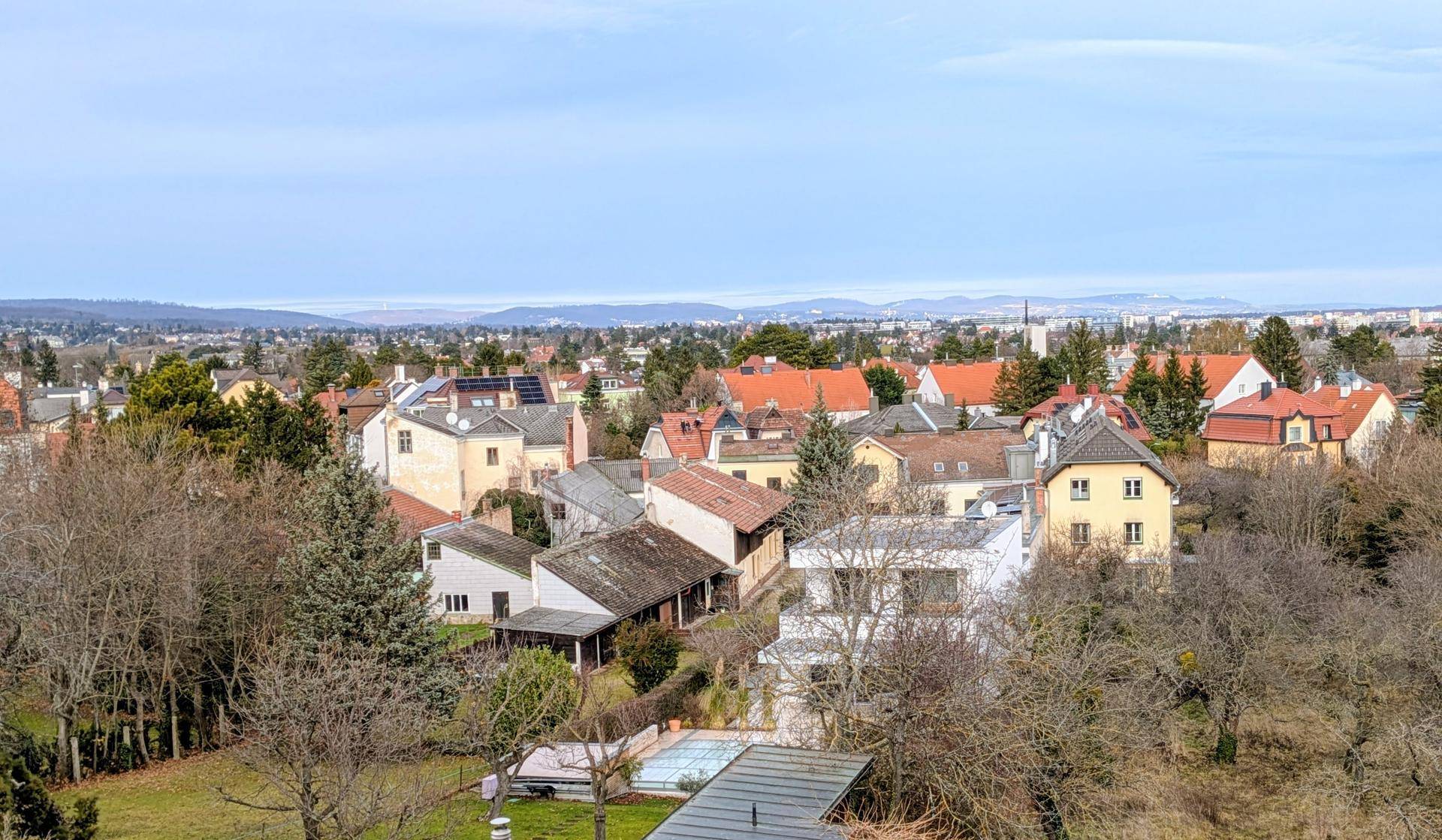 Weitläufiger Blick über eine Wohnsiedlung mit vielen Bäumen und einem kleinen Pool in der Ferne.