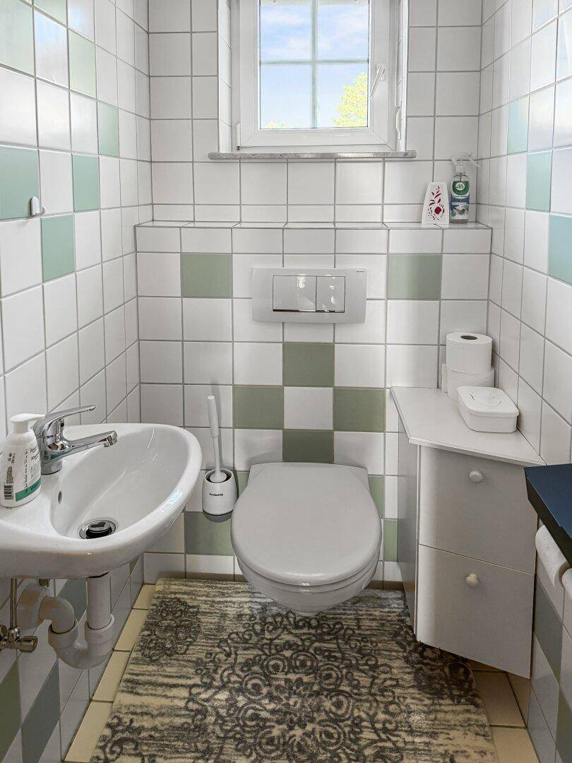 Gäste-WC mit Wand-WC, Waschbecken und hellgrünen Fliesen.