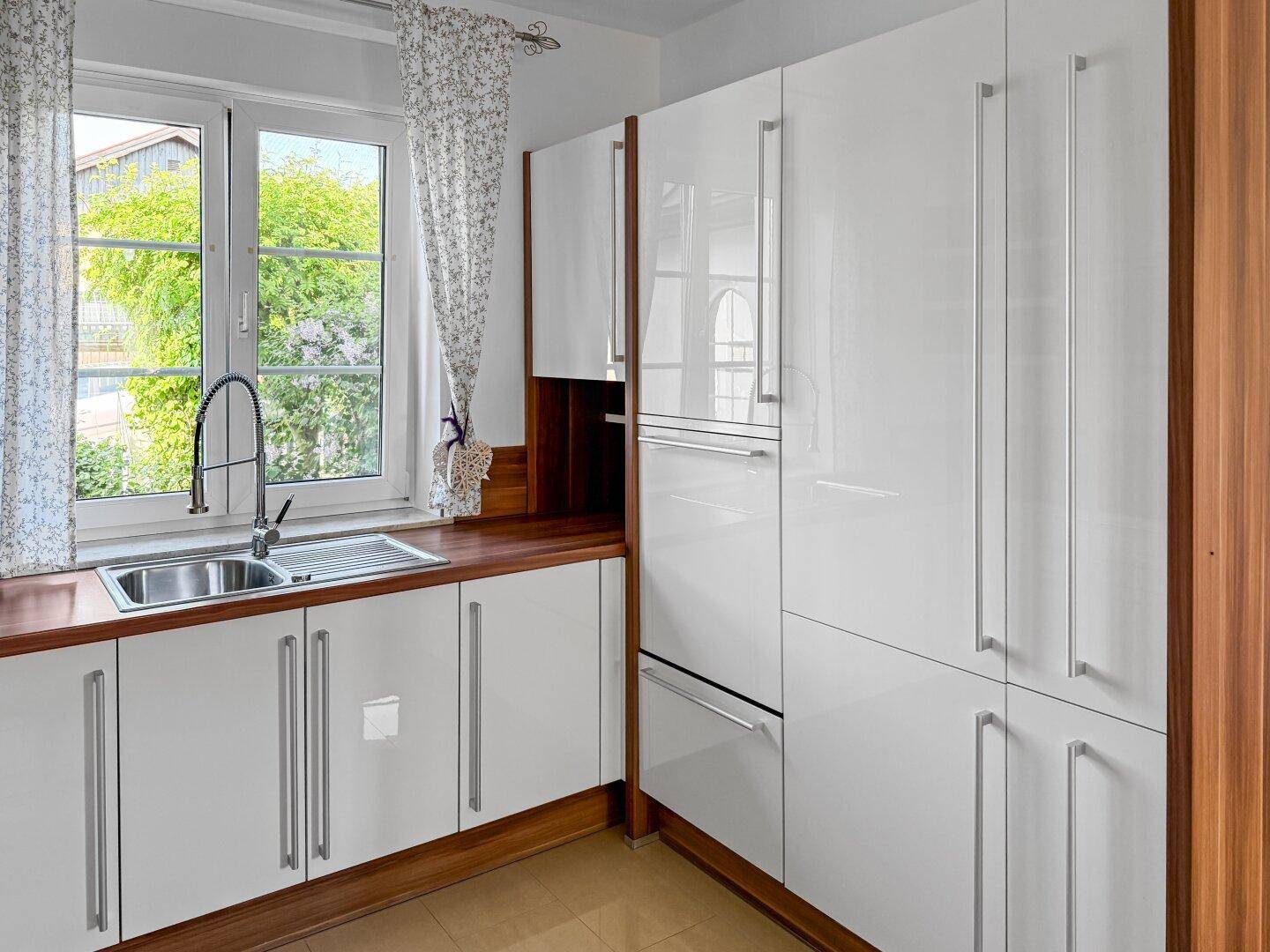 Helle Küche mit Spülbecken unter dem Fenster und integriertem Kühlschrank.