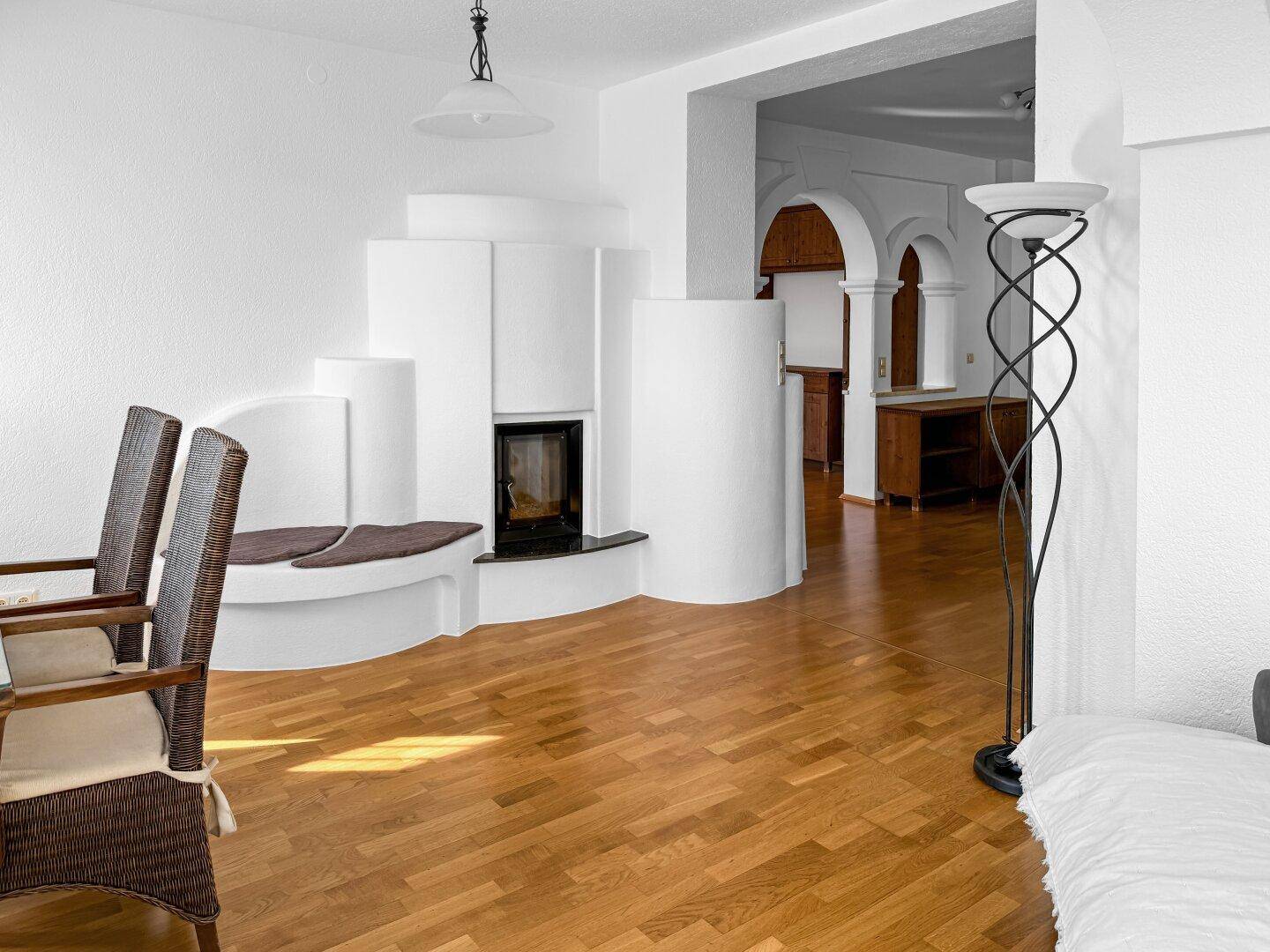 Wohnzimmer mit modernem Kaminofen und Holzboden, offen zu weiteren Räumen.