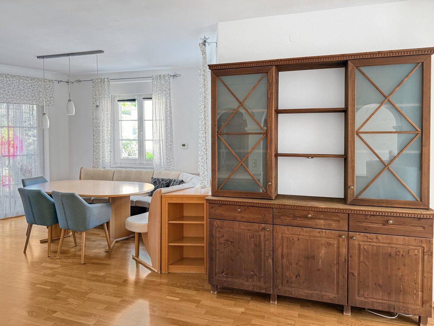 Essbereich mit Holzboden und einem traditionellen Holzschrank im Hintergrund.