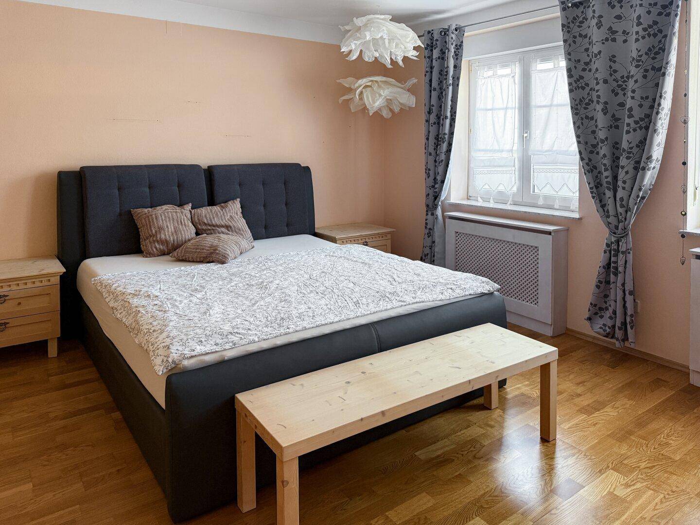 Schlafzimmer mit Doppelbett, Holzboden und Fenster mit Vorhängen.
