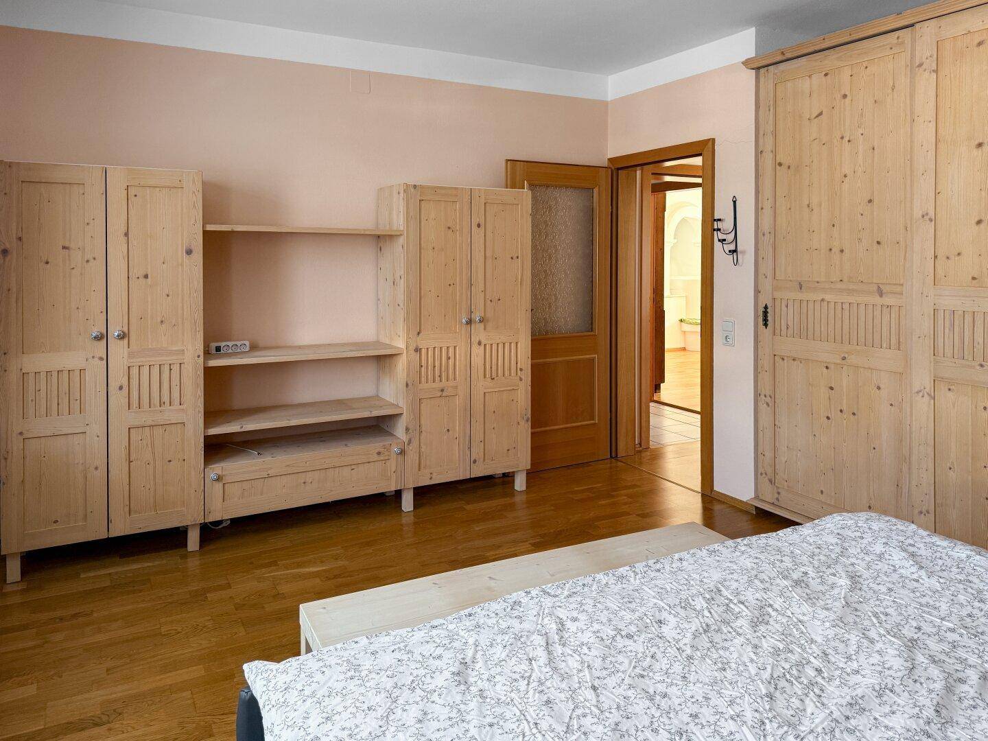 Schlafzimmer mit Holzboden und mehreren Holzschränken, Tür zum Bad.