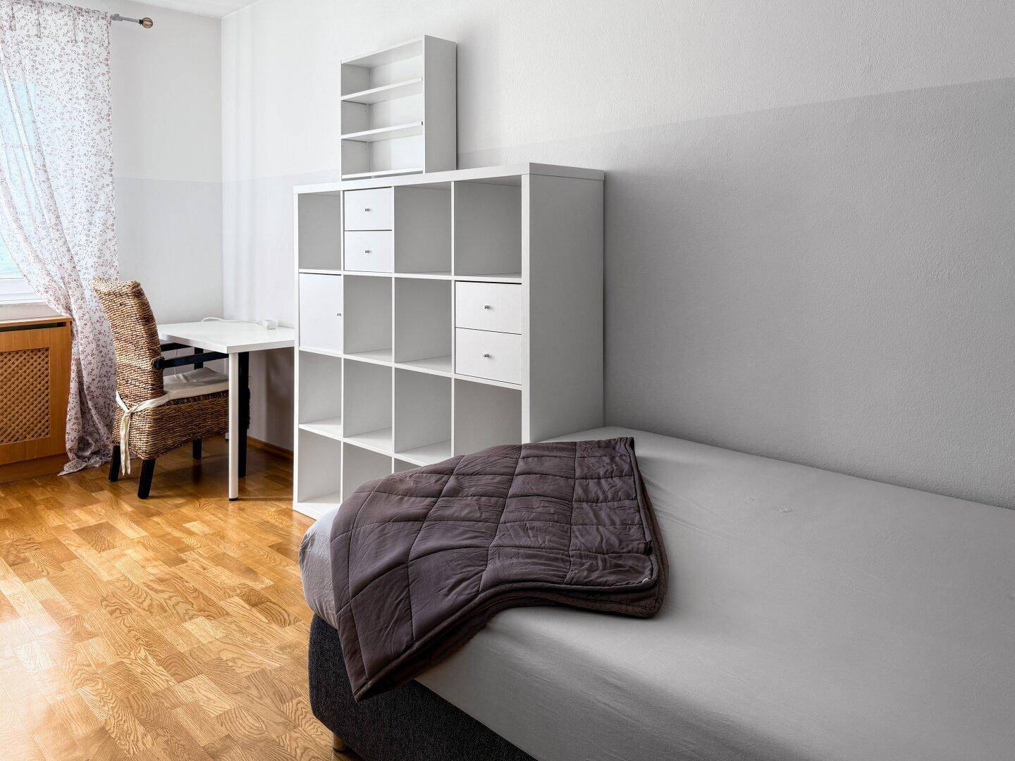 Gemütliches Schlafzimmer mit Einzelbett, Holzboden und weißem Regalsystem.