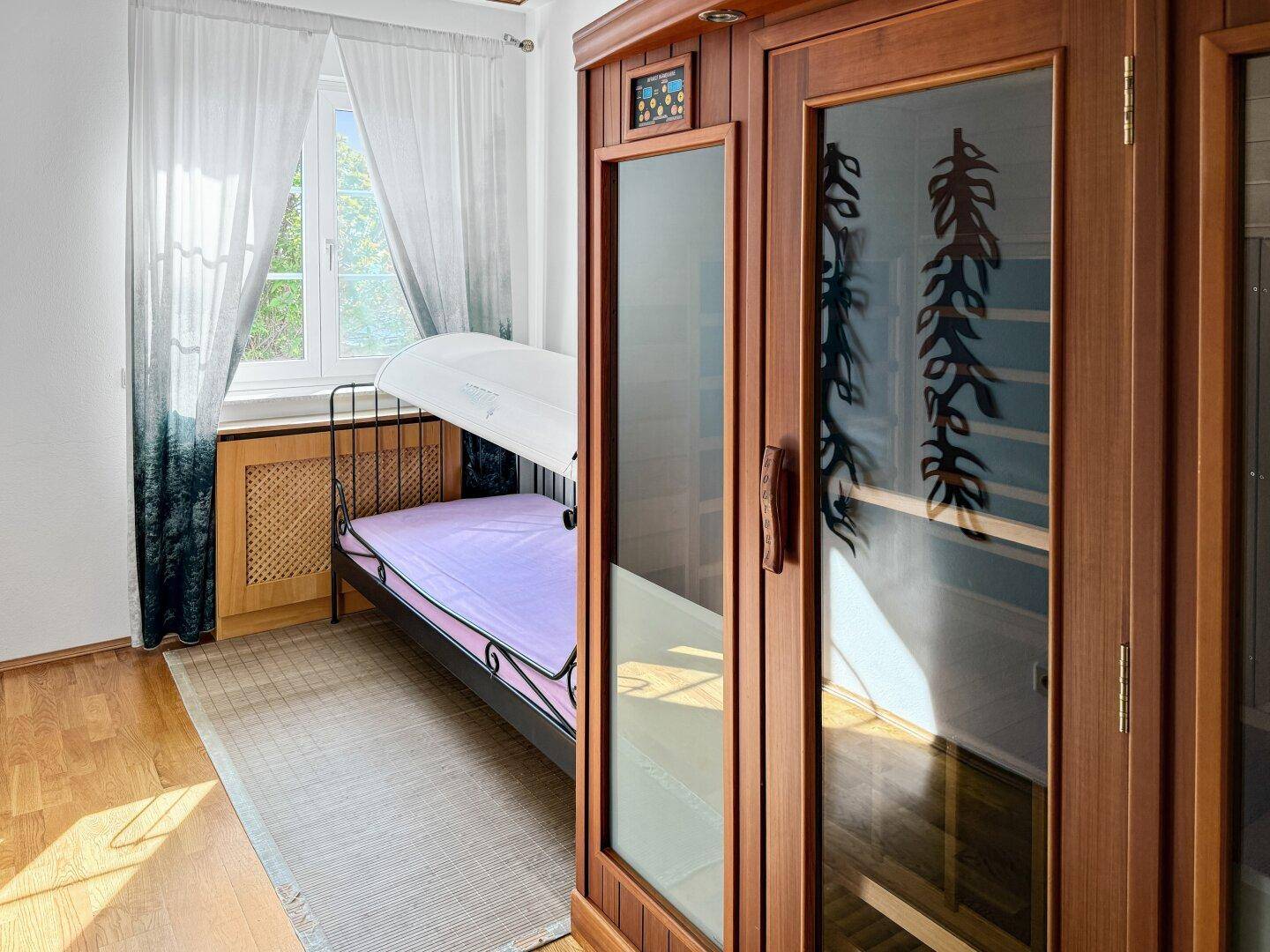 Schlafzimmer mit Einzelbett, Holzboden und integrierter Infrarotkabine.