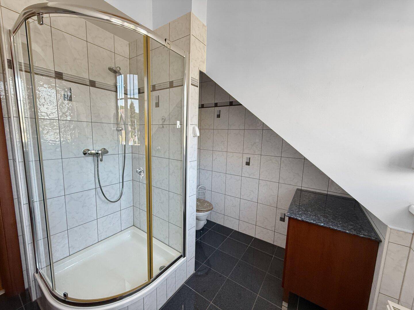 Badezimmer mit Duschkabine, WC und Fliesenboden unter der Dachschräge.