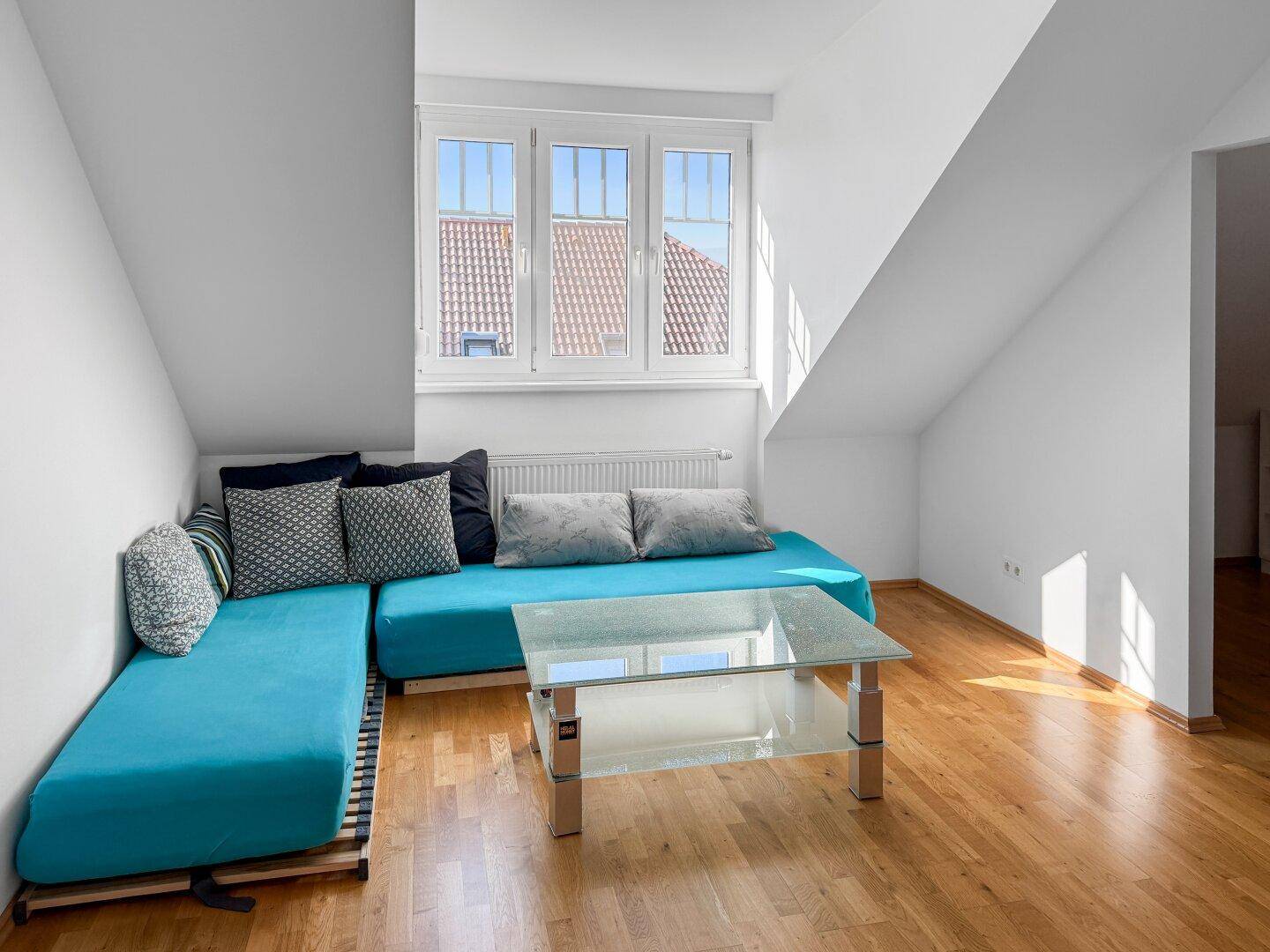 Helles Zimmer im Dachgeschoss mit Sofa, Couchtisch und Holzboden.
