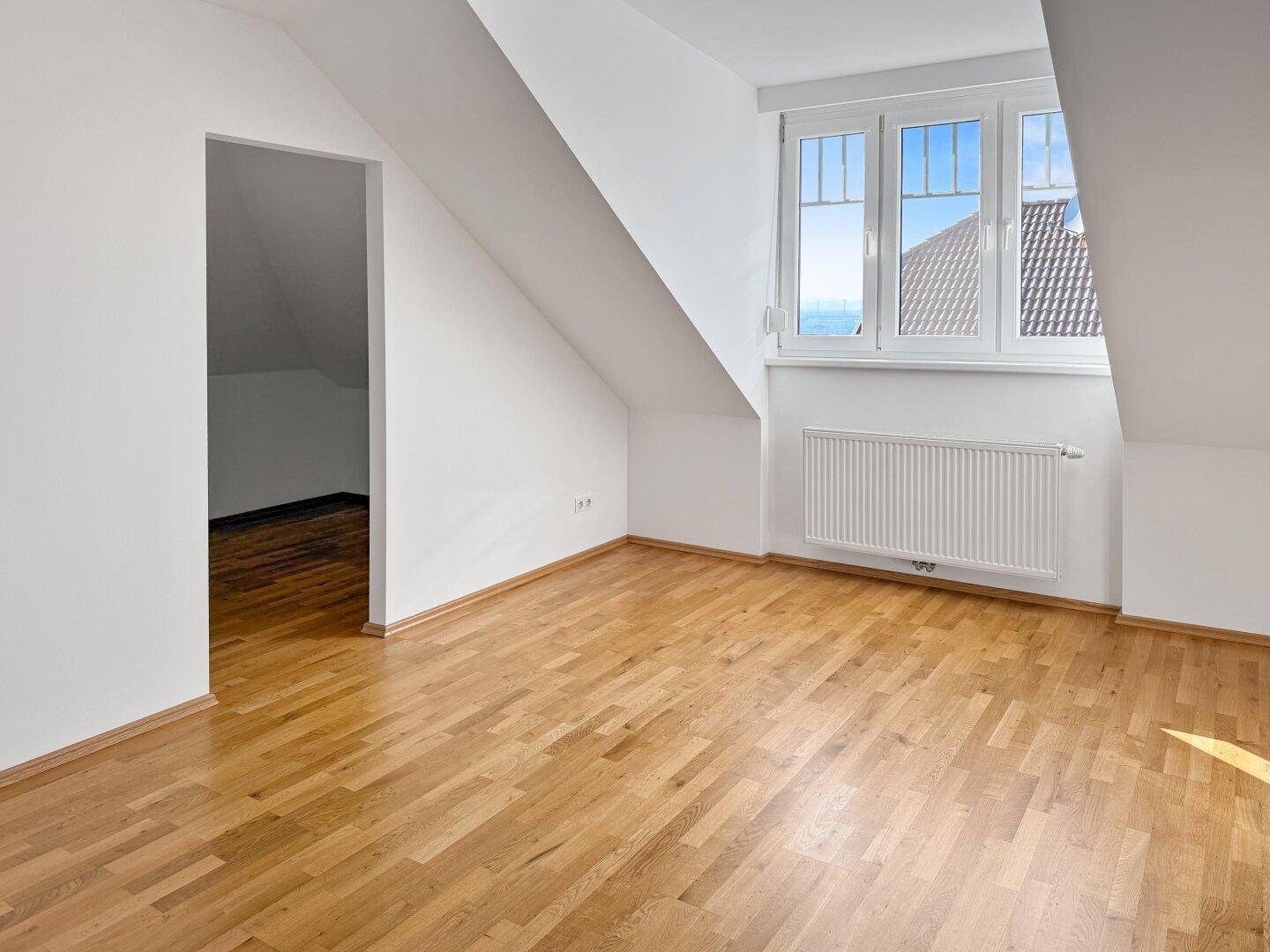 Geräumiges Zimmer im Dachgeschoss mit Holzboden und viel Tageslicht.