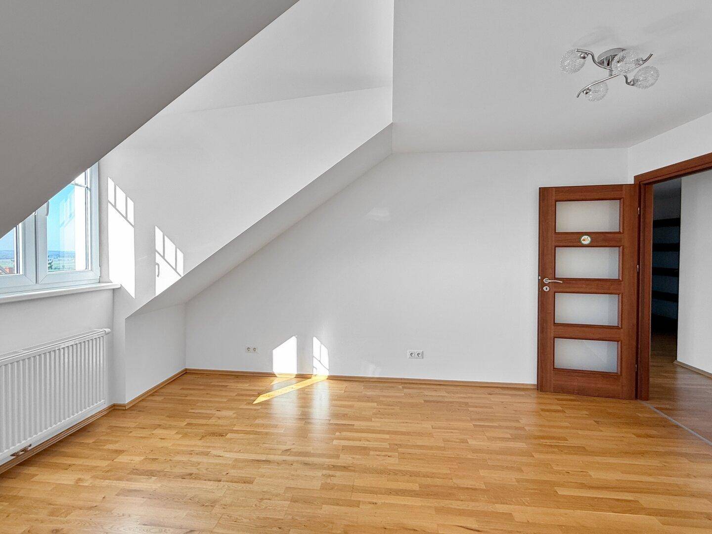 Heller Raum im Dachgeschoss mit Holzboden, Dachschräge und Holztür.