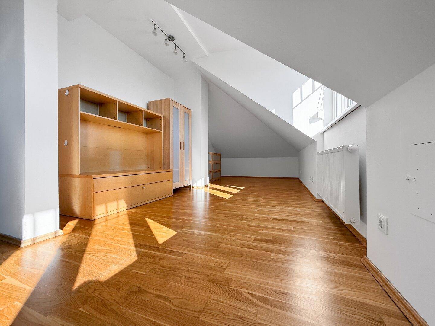 Großzügiger Raum im Dachgeschoss mit Holzboden, Dachschräge und Holzmöbeln.