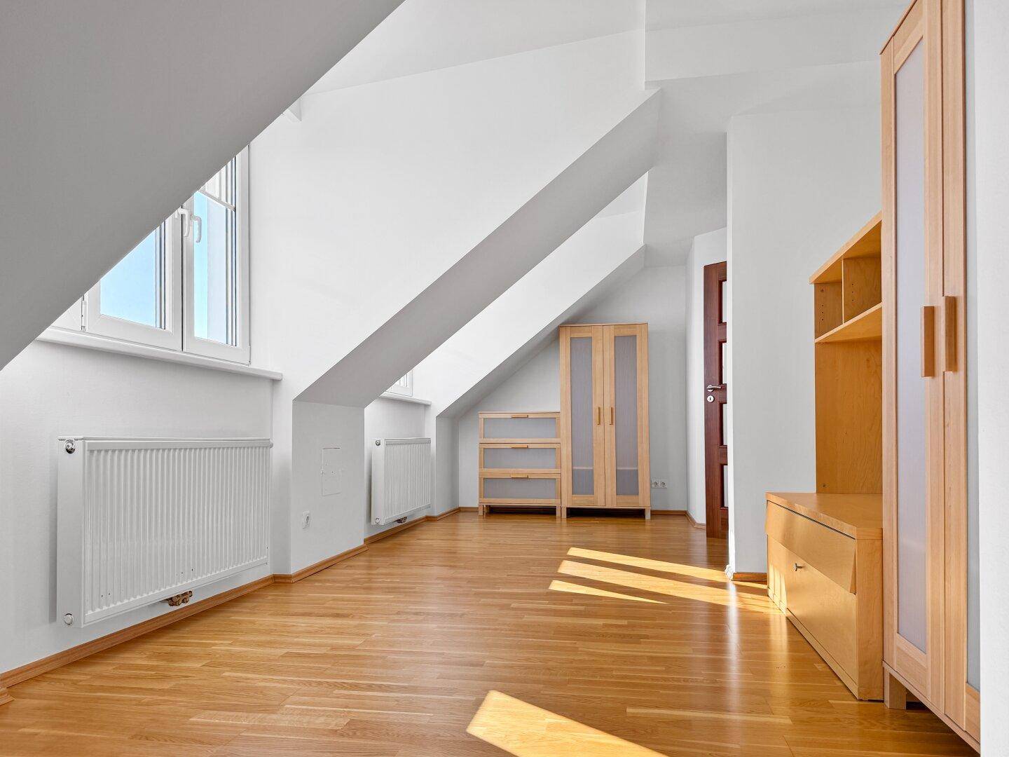 Helles Zimmer im Dachgeschoss mit Holzboden, Dachschräge und Heizkörper.